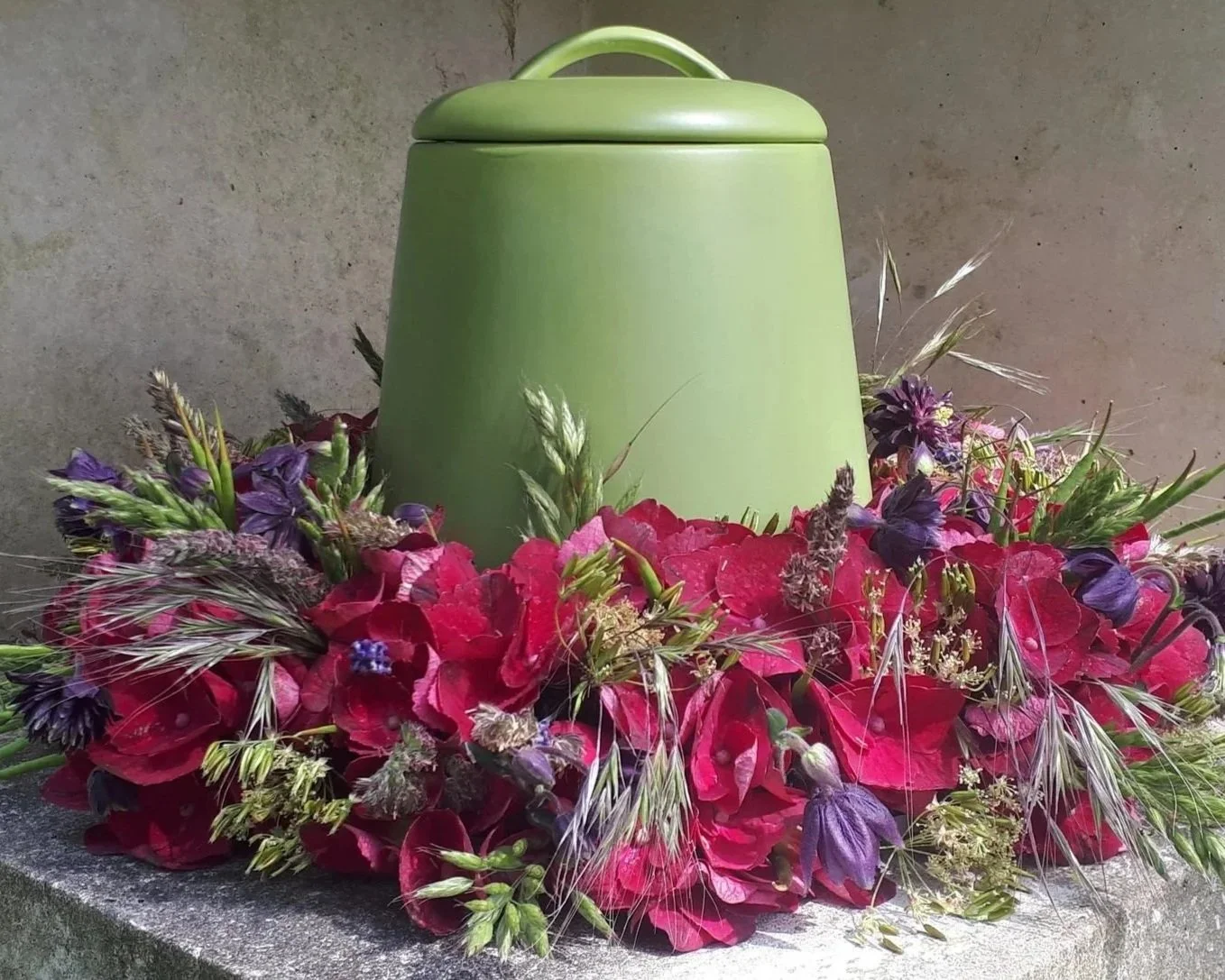 Rouwarrangement rond groene urn met donkerroze en paarse bloemen.jpg