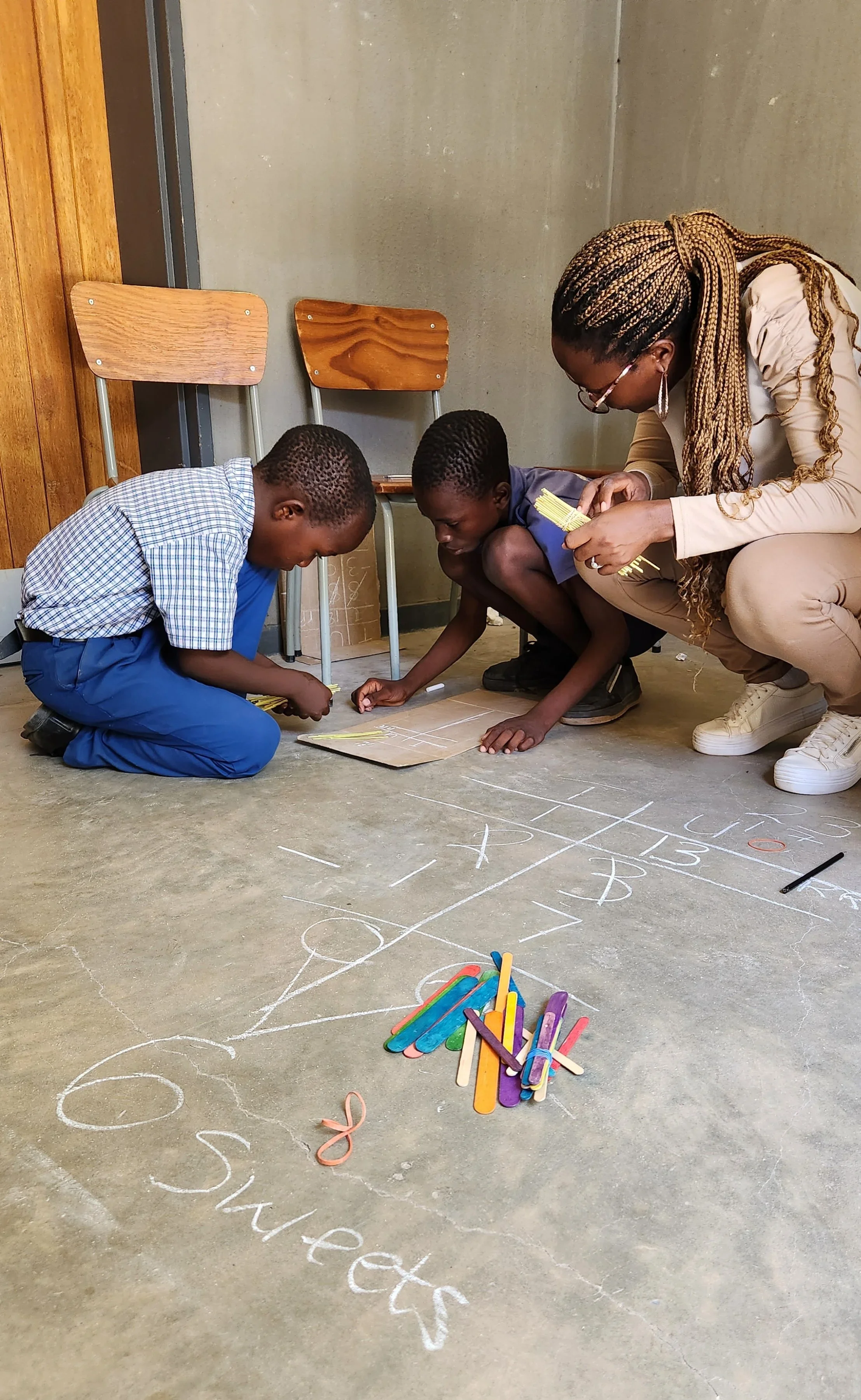 A woman and two children are writing on the floor with chalk.