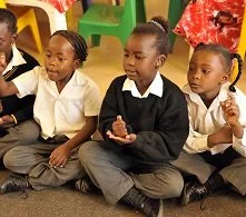 Four young children sitting on the floor, wearing school uniforms, participating in a classroom activity.