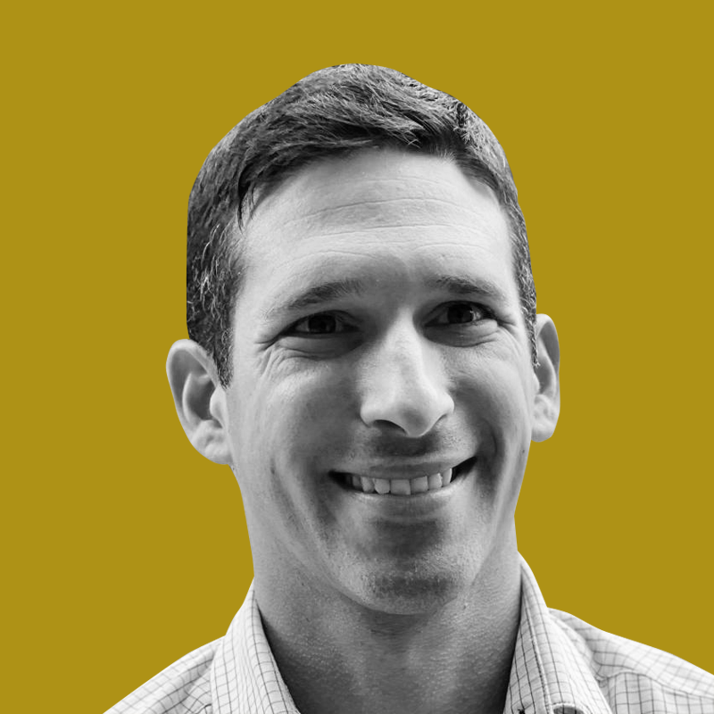 Black and white photo of a smiling man with short hair, wearing a checkered collared shirt, against a yellow background.