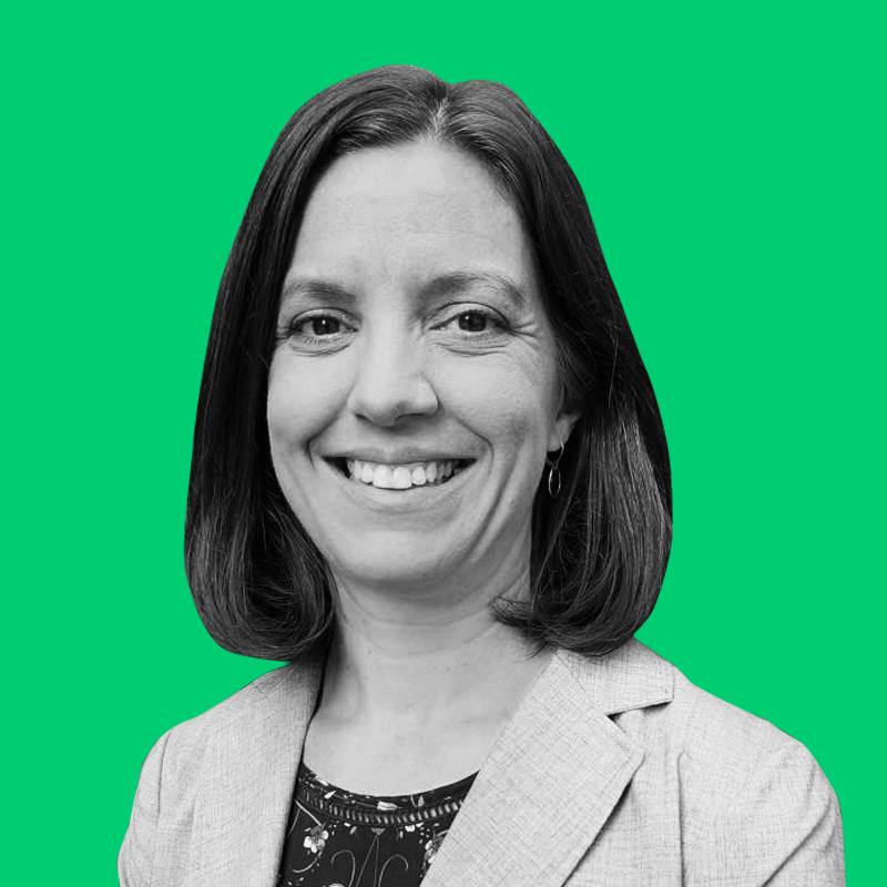 Black and white photo of a woman with shoulder-length hair, smiling, wearing a blazer and a patterned top, against a bright green background.