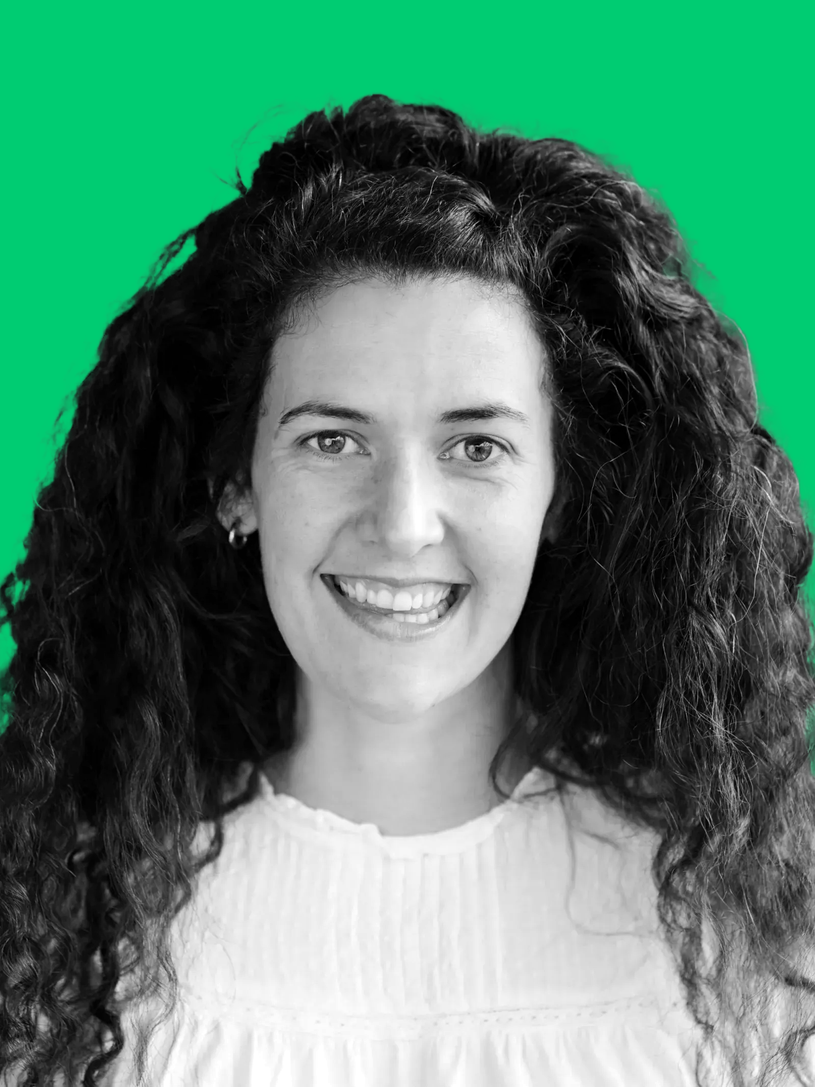 A black-and-white portrait of a woman with long, curly hair smiling, background is green.