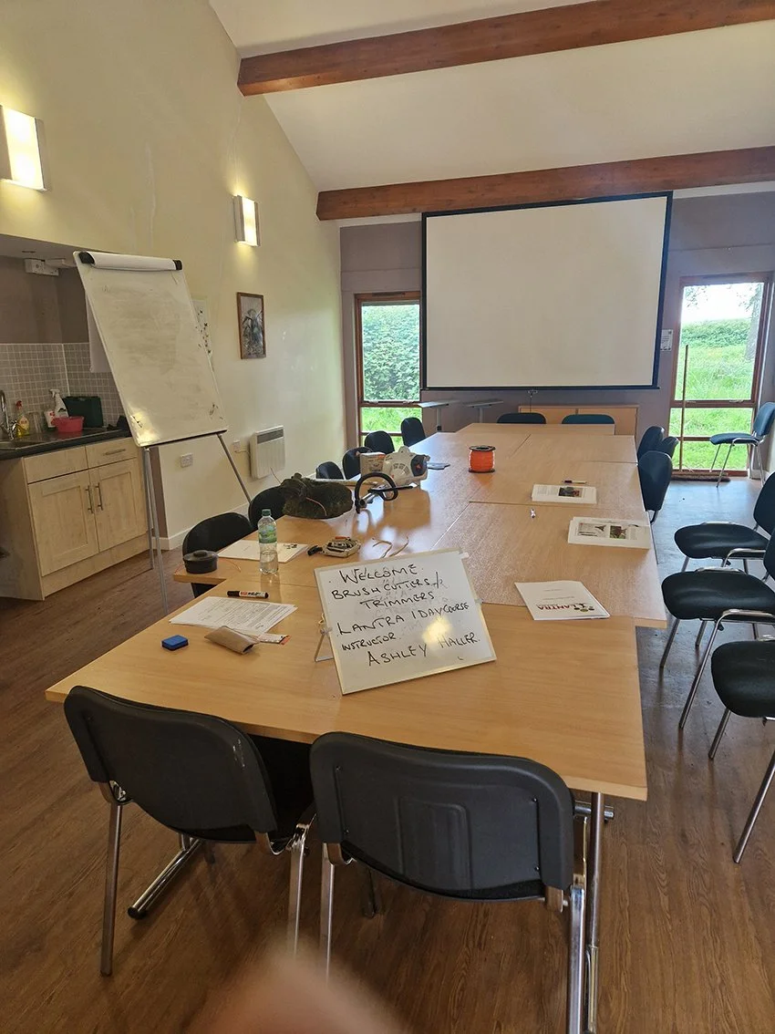 A conference room with a long table arranged for a training session, with chairs around it, a whiteboard, and a projector screen. There are windows letting in natural light and a sign on the table welcoming attendees.