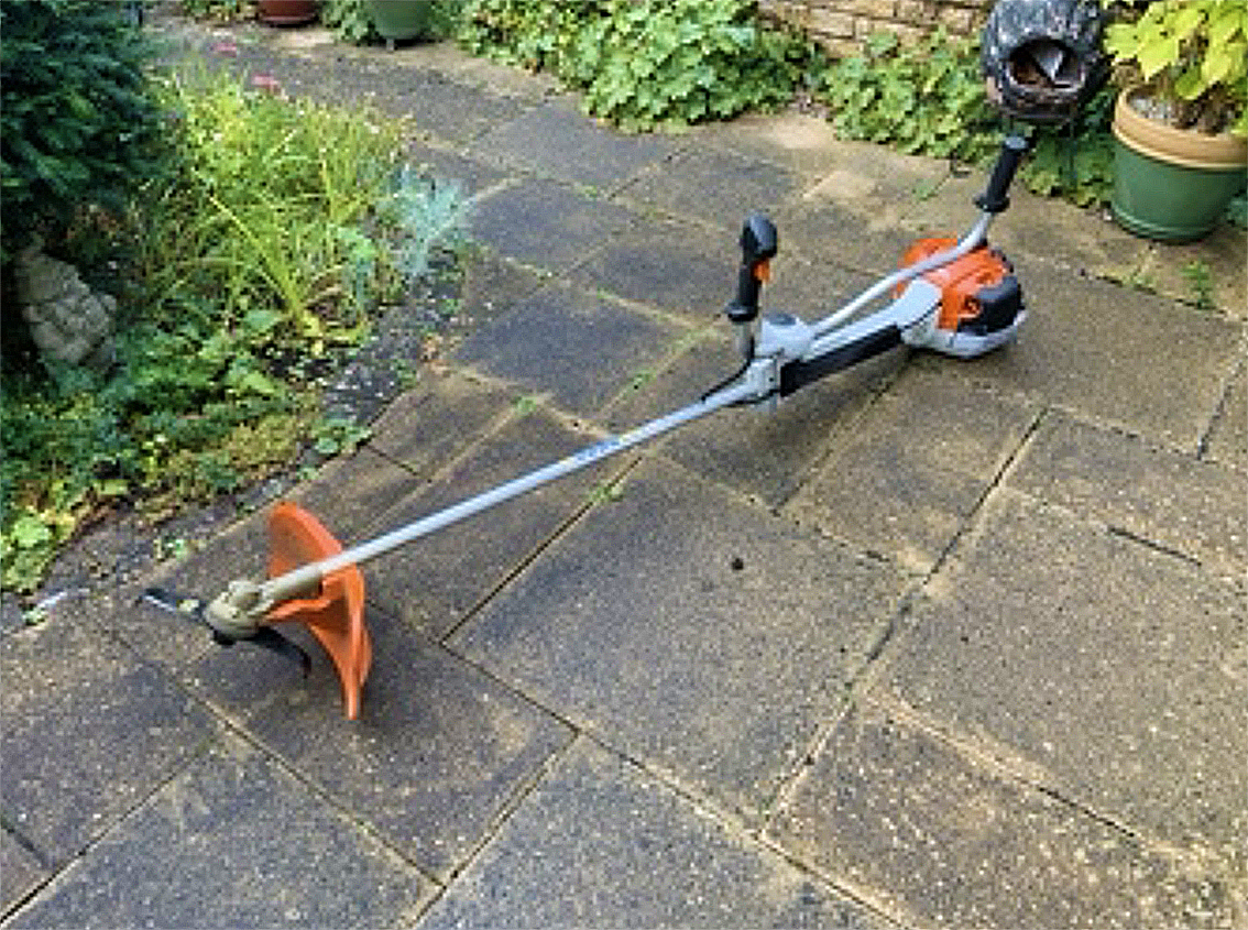 A garden with patio paving and a cordless grass trimmer lying on the ground.