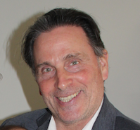 Portrait of a smiling man with dark hair and a beard, wearing a suit and tie.