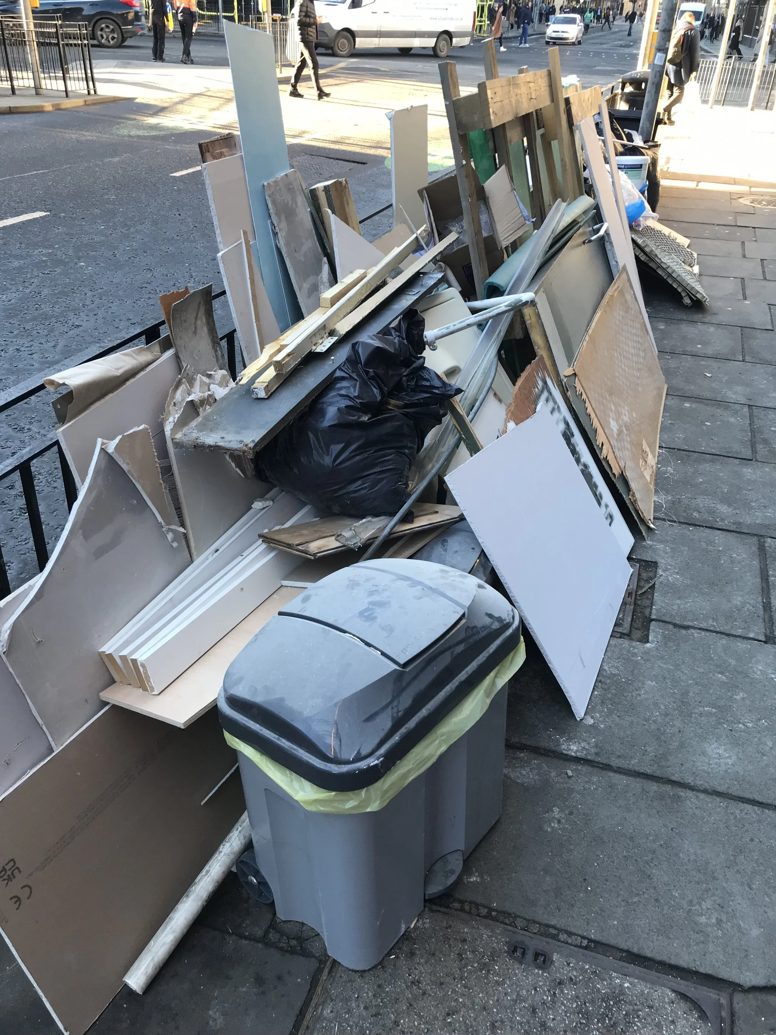 A pile of demo debris and materials, including drywall, wood, and other building supplies, on an Edinburgh city centre pavement with a city street and pedestrians in the background.
