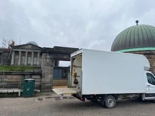 Ootnoo's white Luton van parked in front of the old Edinburgh Observatory at Calton Hill, with a green-domed structure in the background, on a cloudy day.