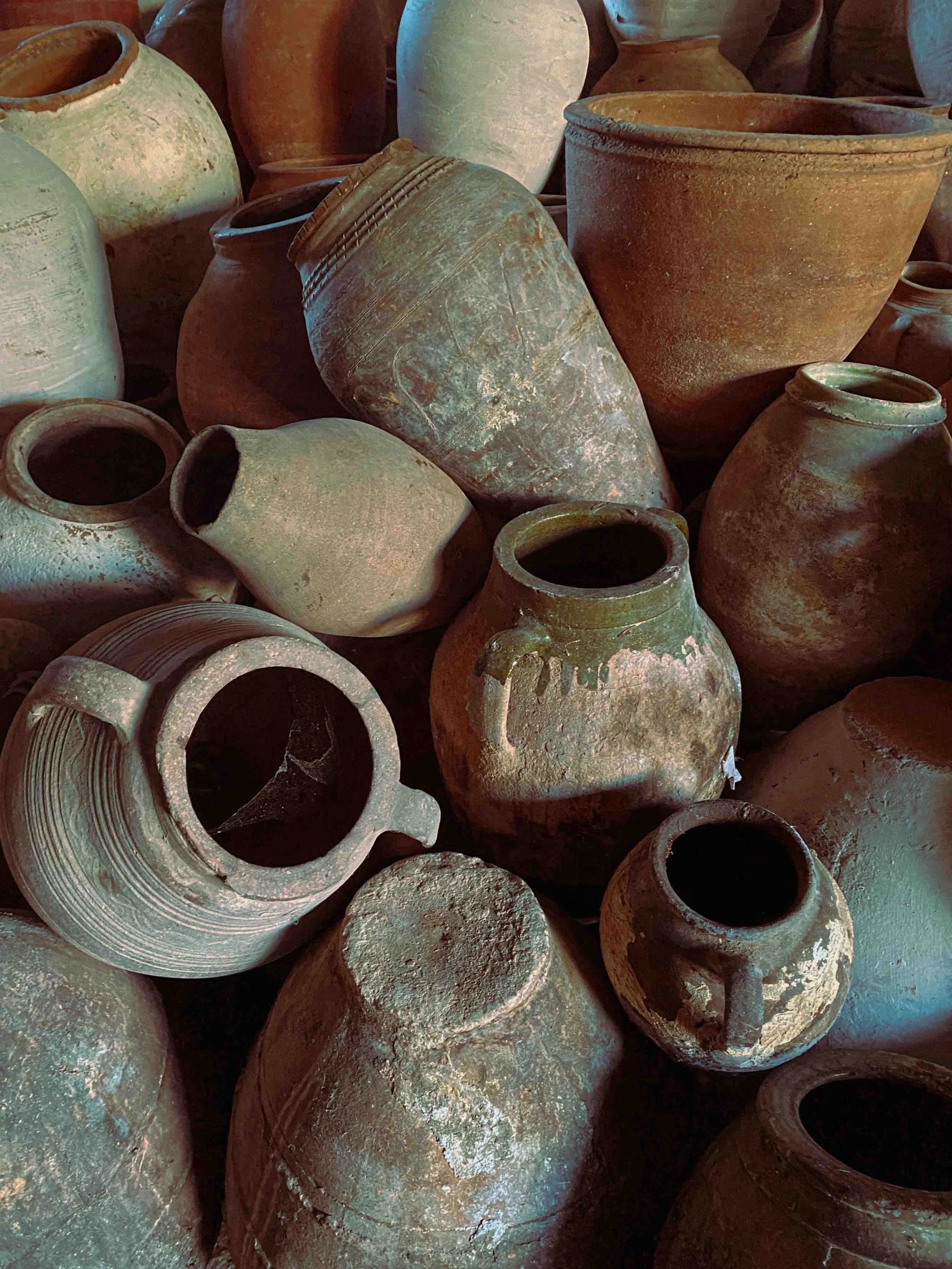 A collection of old, weathered clay pots and jars stacked together, showing various shapes, sizes, and earthy tones.