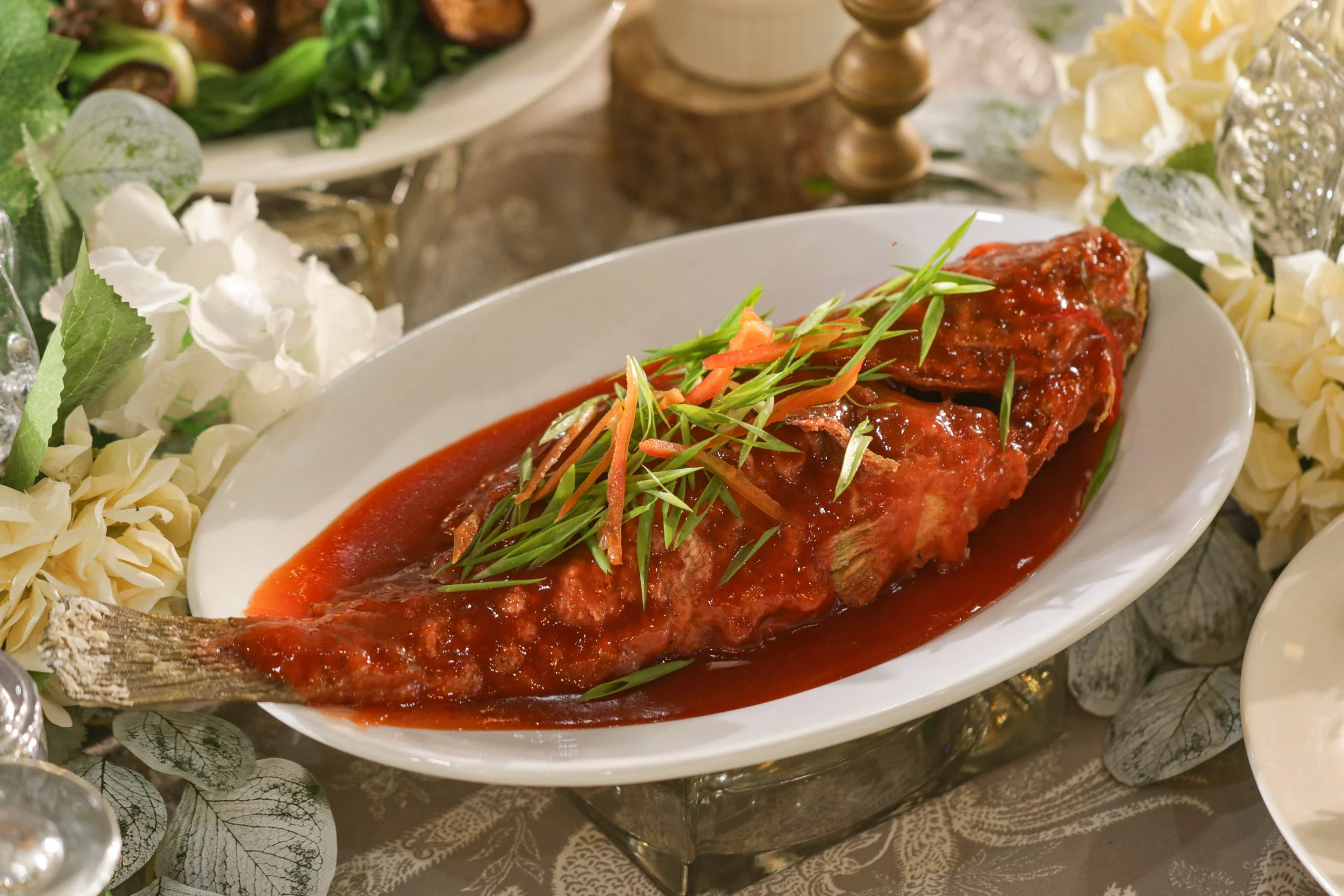 A cooked fish with a red sauce garnished with green herbs, served on a white platter.