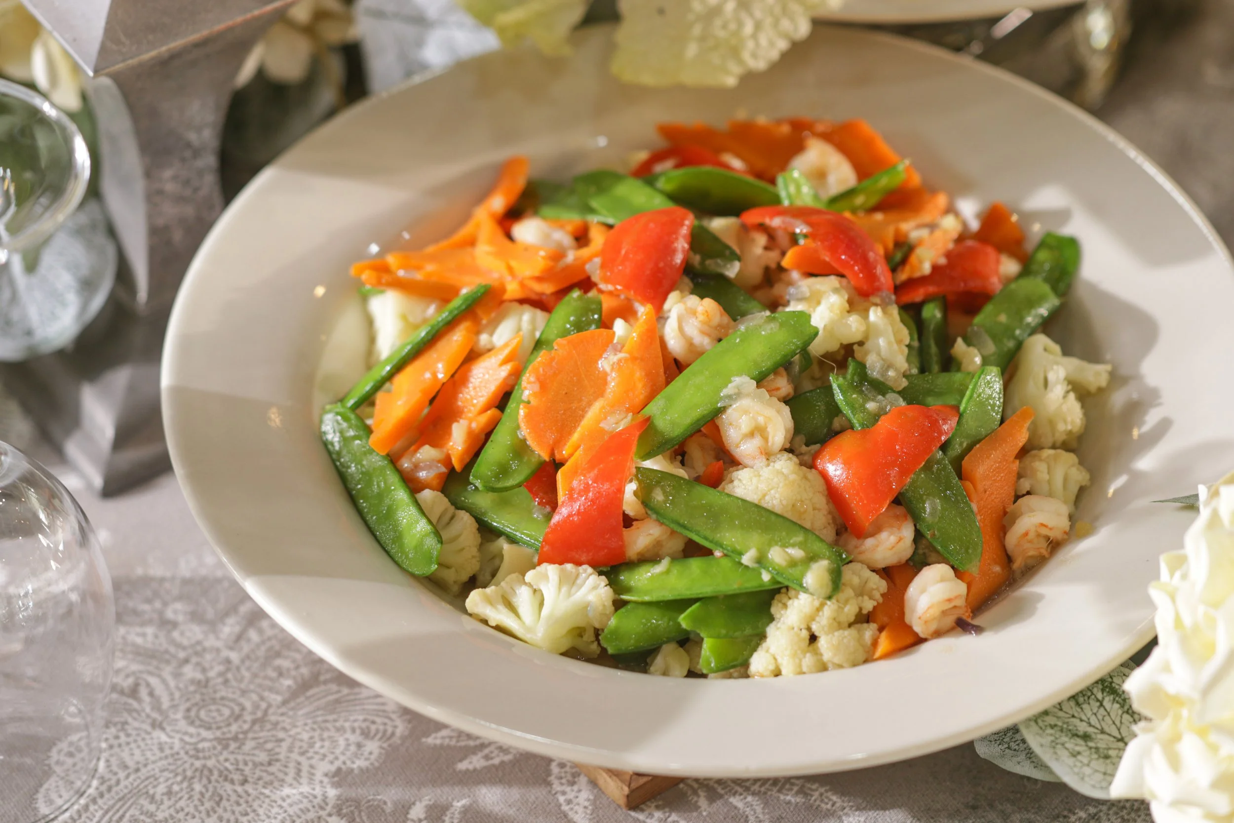 A plate of cooked mixed vegetables including cauliflower, carrots, red bell peppers, and snap peas.