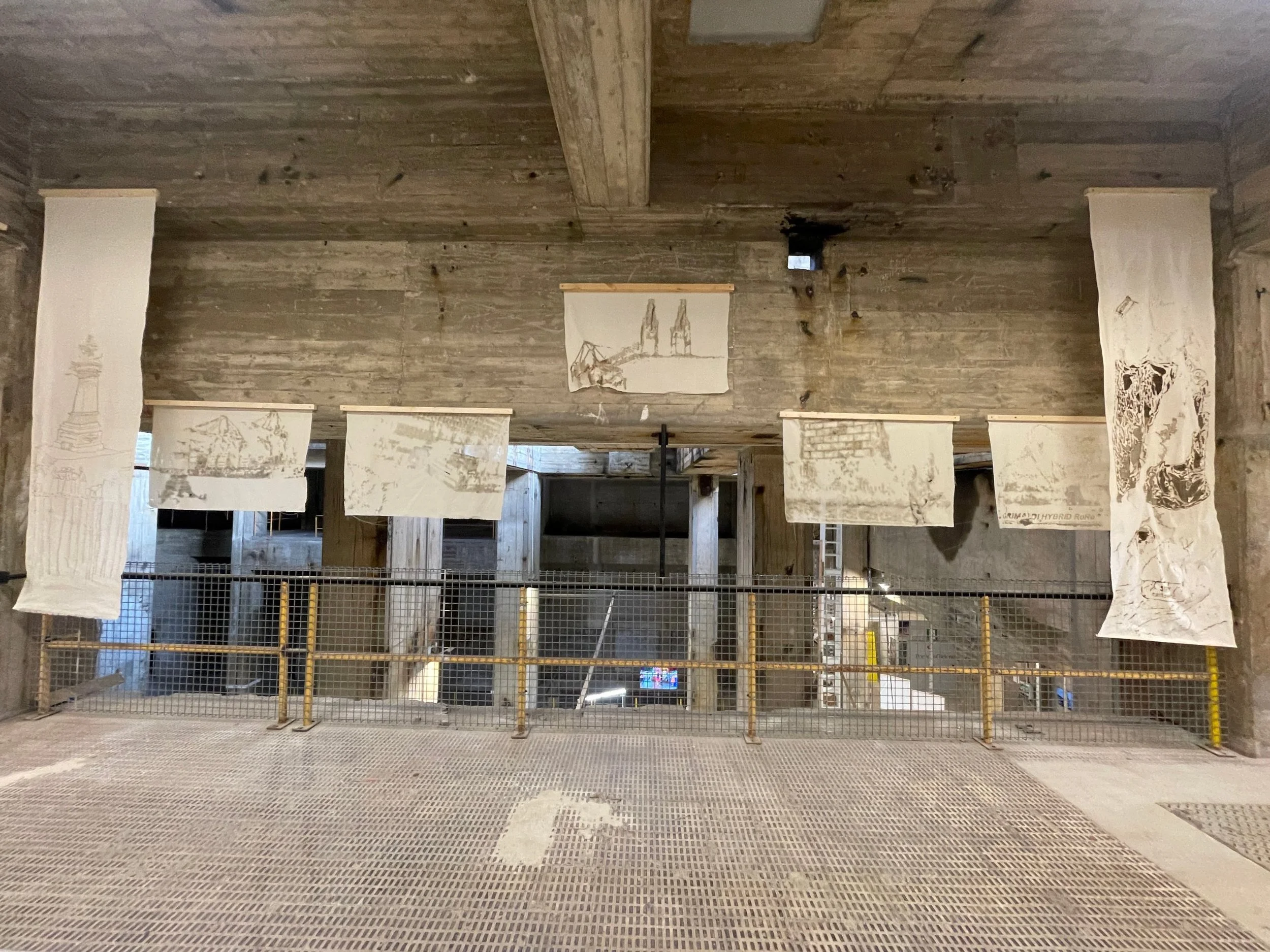 Seven burnt calico pieces from the Revised Cartographies workshop suspended along a gallery balustrade at the UIA World Congress of Architects 2026, Barcelona.