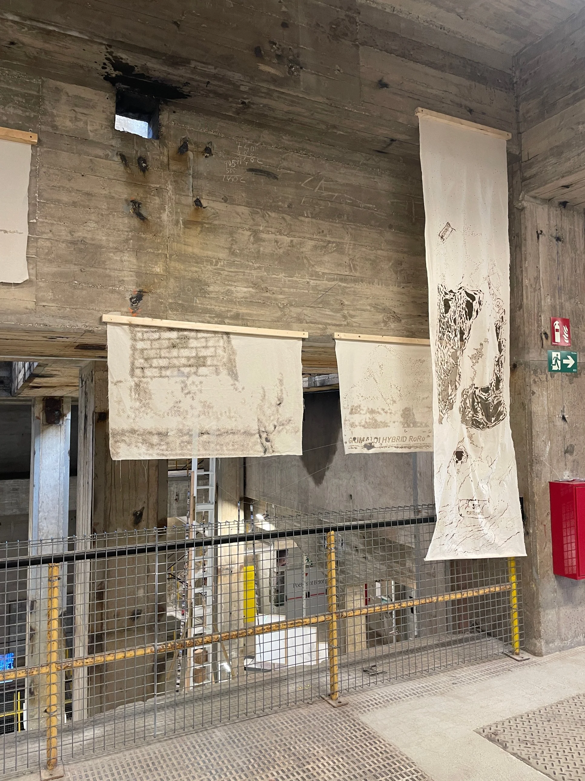 Calico pieces from the Revised Cartographies workshop hanging in a concrete hall, with landscape point clouds burnt into the cloth.