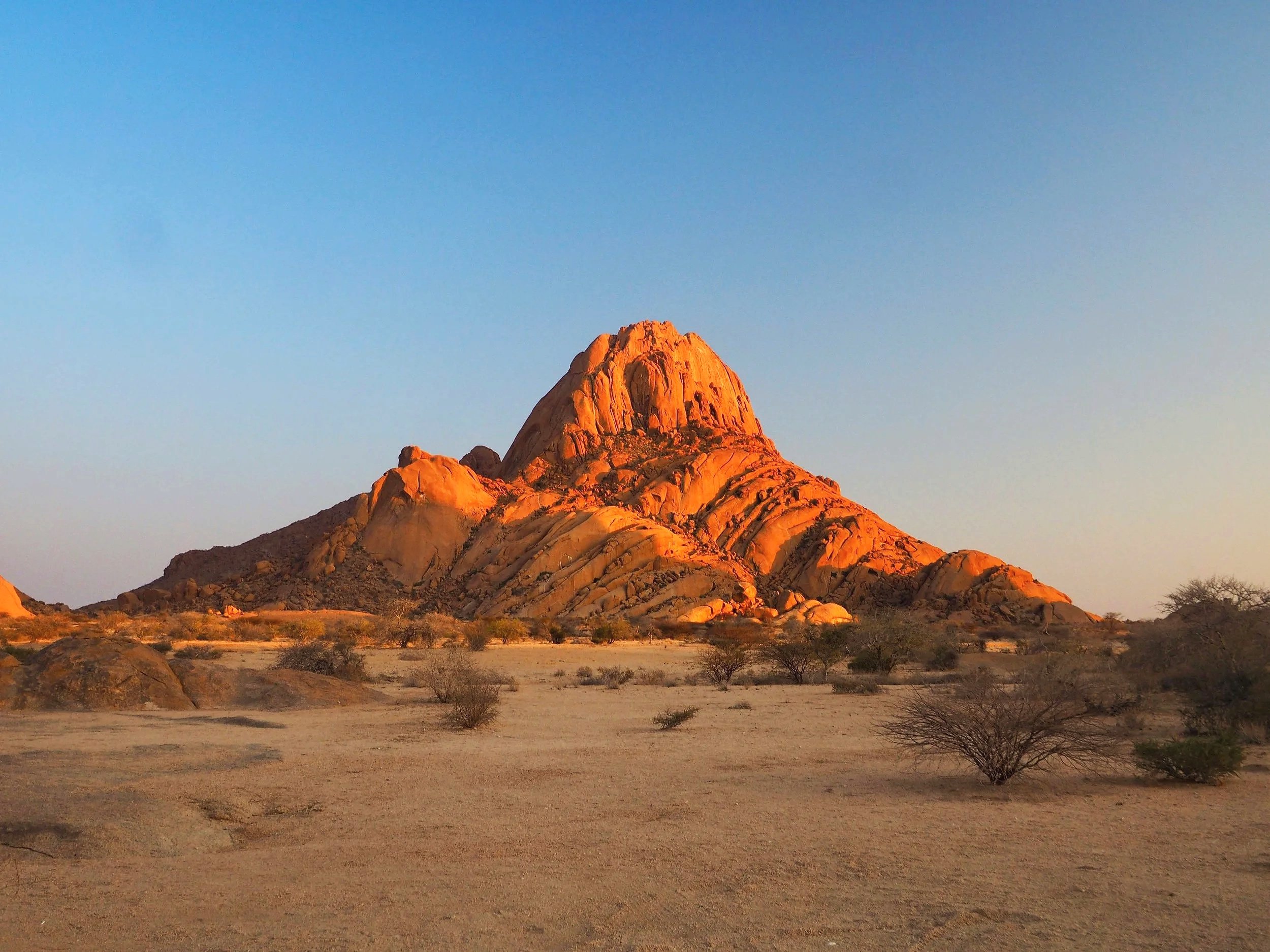 A desert landscape with large red rocks and mountains at sunset, viewed through a natural rock arch