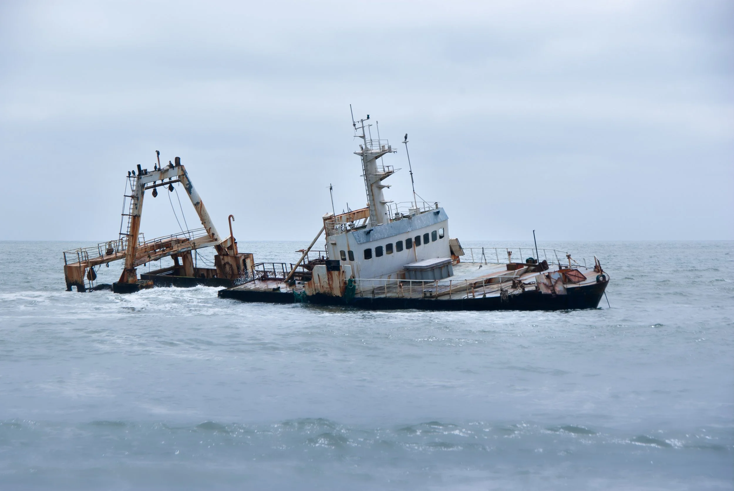 Zeila Shipwreck. A rusted, sunken boat partially submerged in the ocean with waves crashing around it.