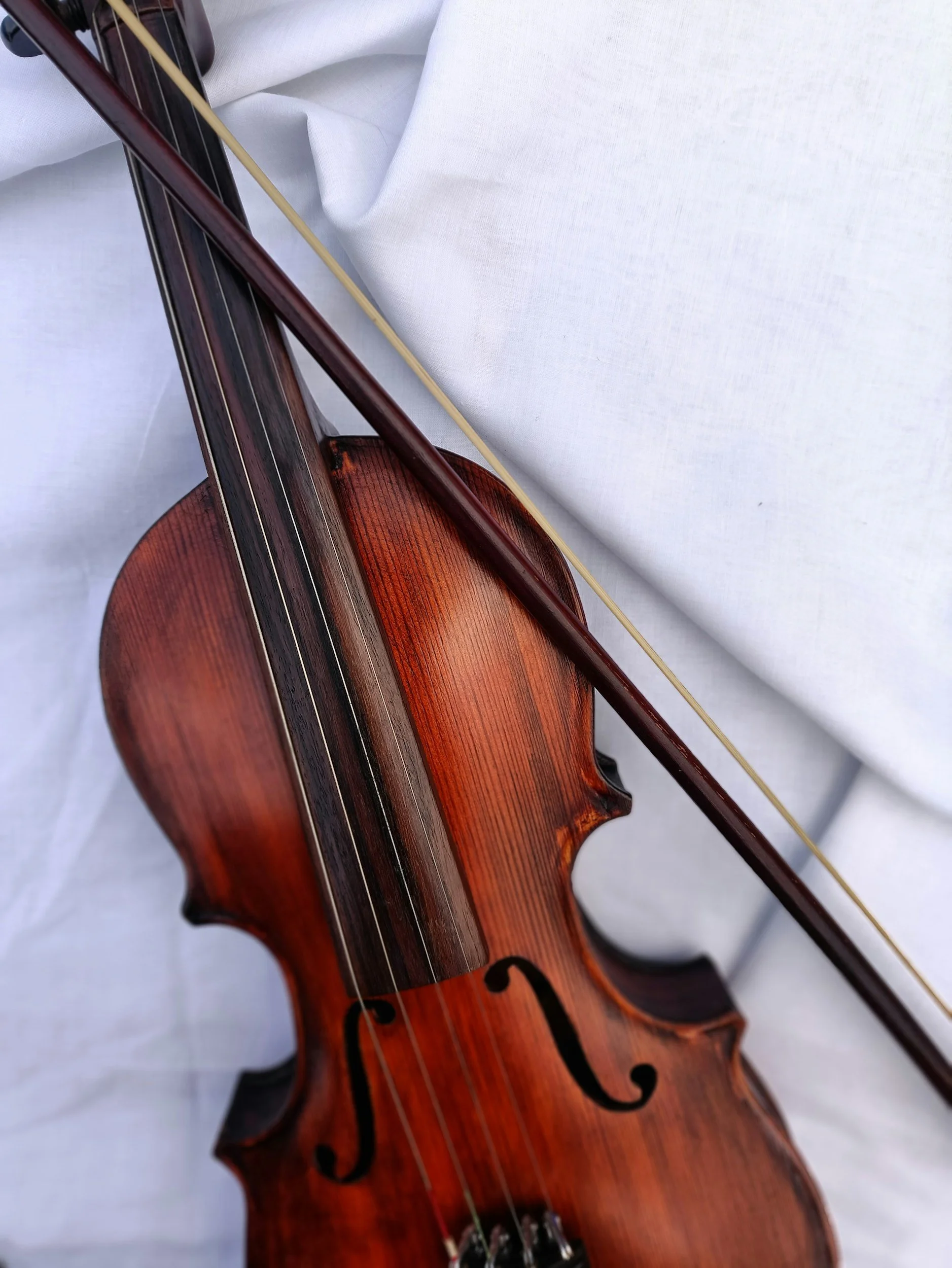 Close-up of a wooden violin with a bow resting on it, placed on a white fabric background.