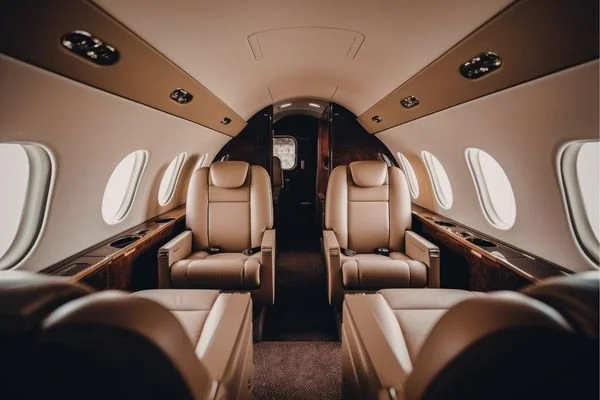 Interior of a private jet with beige leather seats and wood accents.