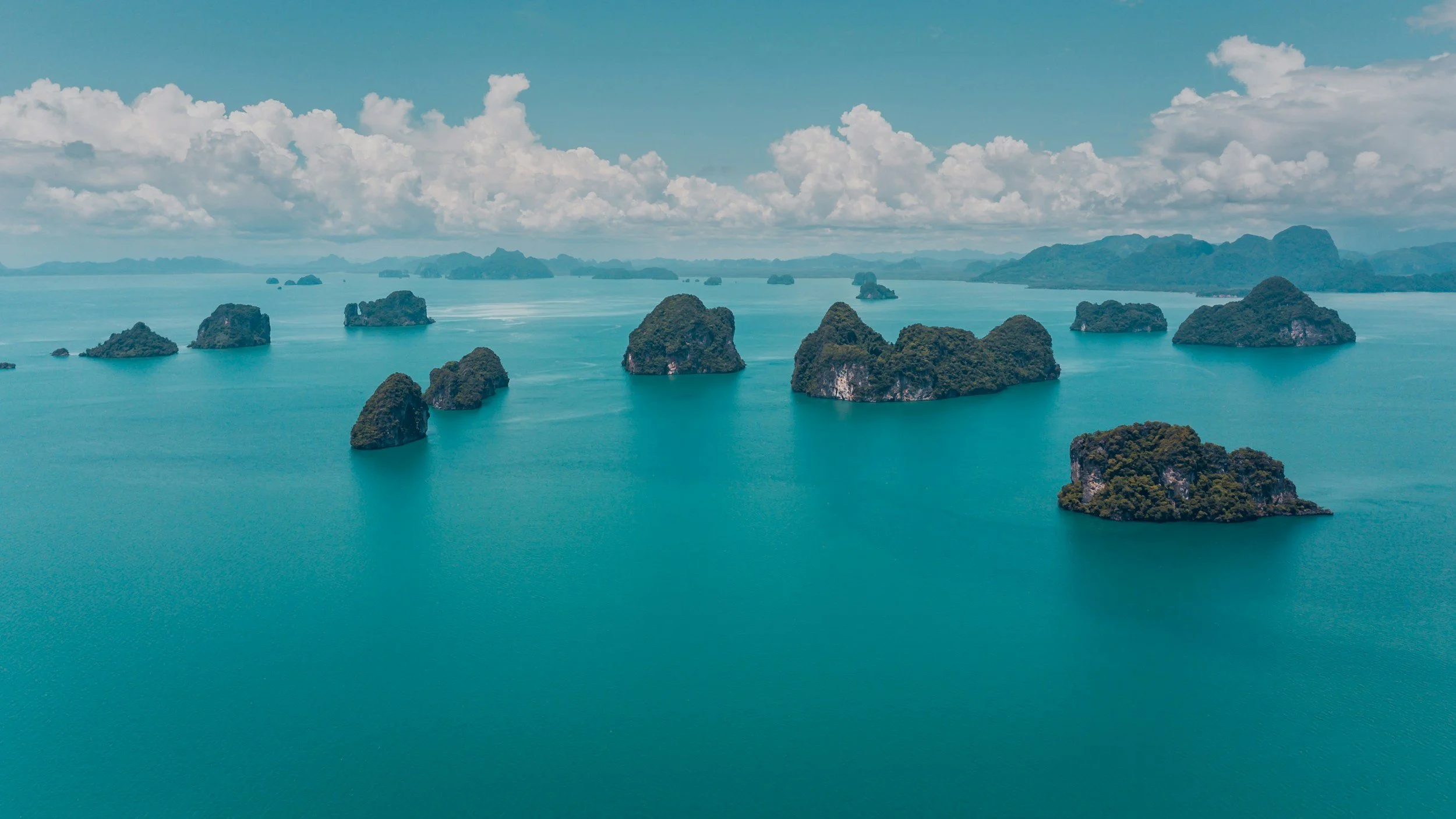 Aerial view of numerous green islands scattered in a calm, blue body of water under a partly cloudy sky.