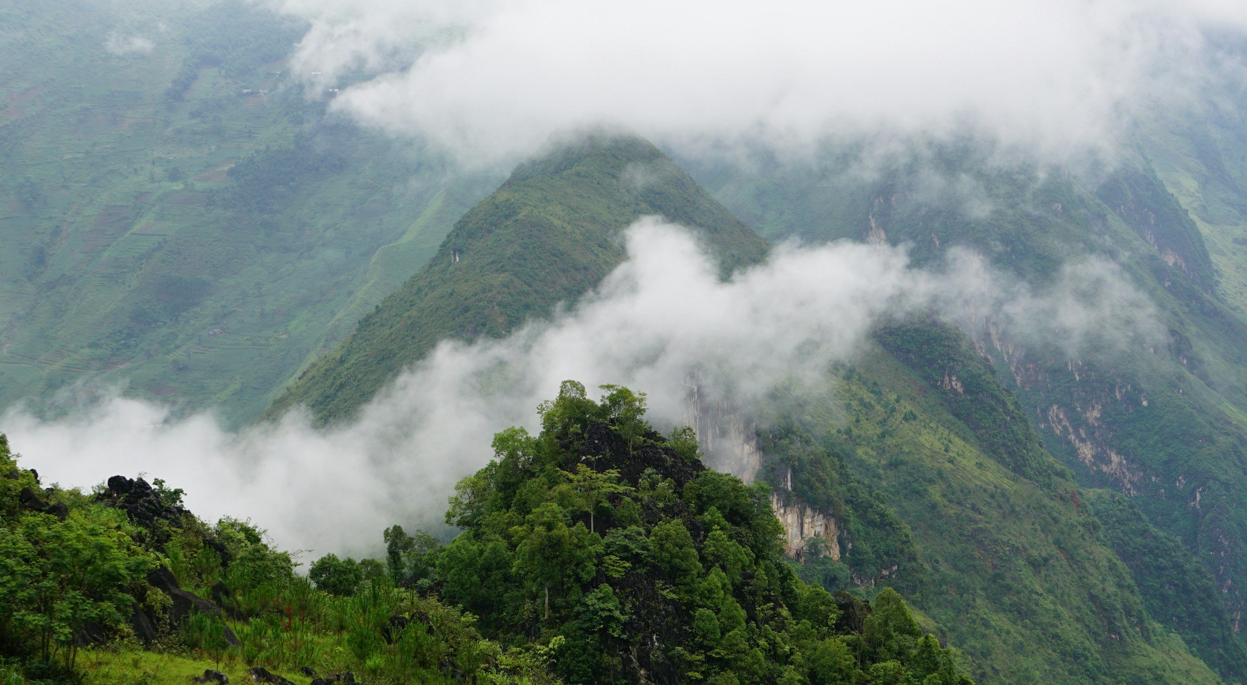 Lush green mountains with clouds and mist surrounding them.