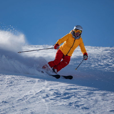 Skier in a yellow jacket and red pants skiing down a snowy slope.