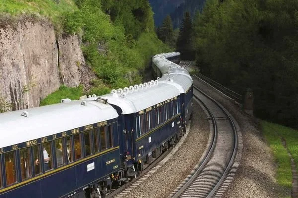 A vintage blue and white train traveling through a lush, green forested area on curved tracks.