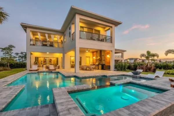 Modern two-story house with a backyard pool and spa during sunset.