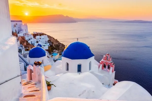 Sunset over Santorini with blue-domed churches and white buildings overlooking the sea.