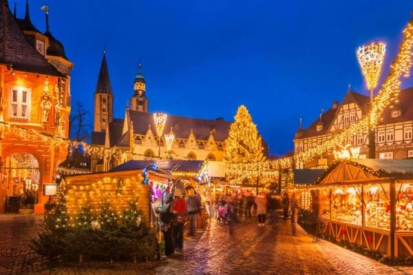 Christmas market with festive lights, market stalls, and a church in the background at night.