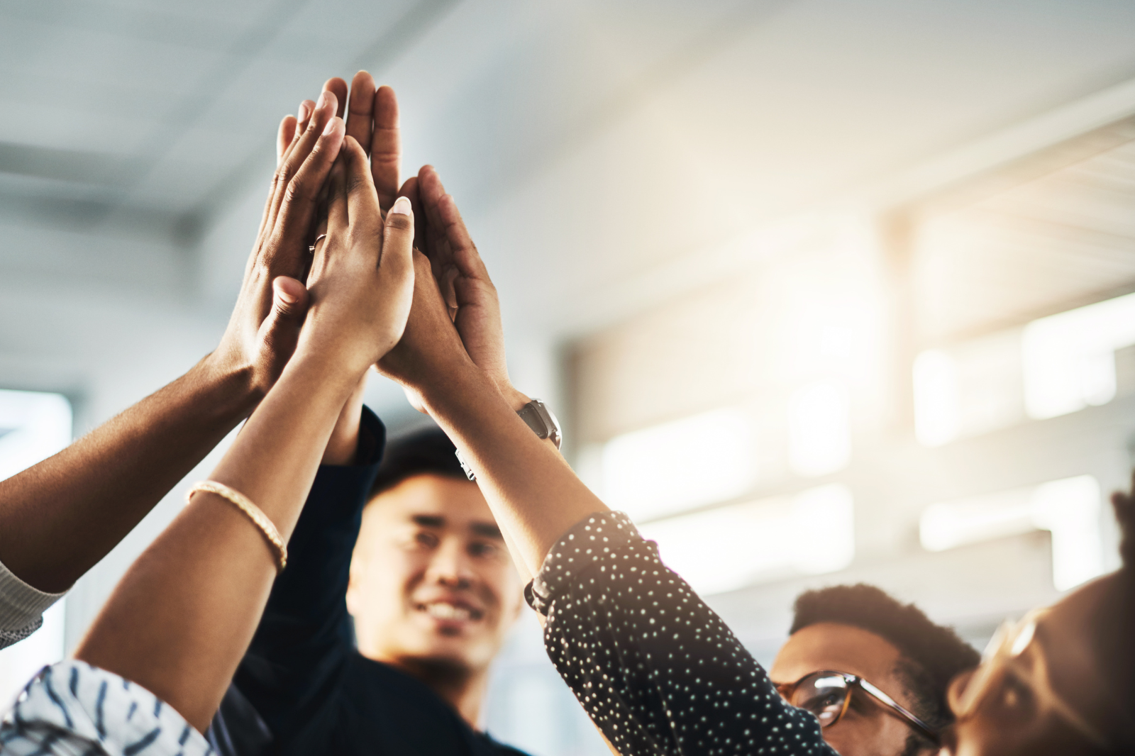 Groupe de personnes se félicitant avec des mains superposées, dans un intérieur lumineux.