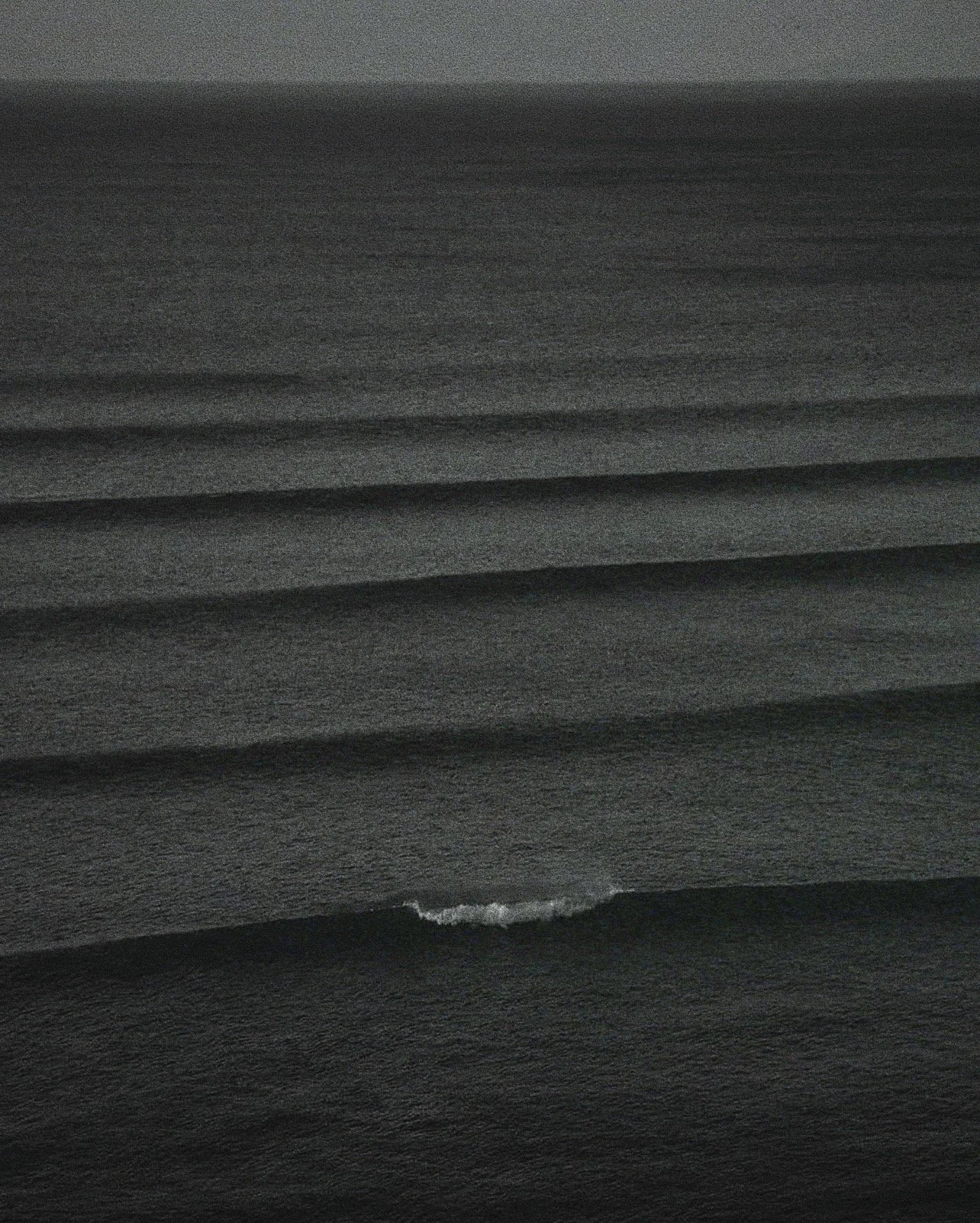 Black sand beach with gentle waves and a small white foam at the shoreline