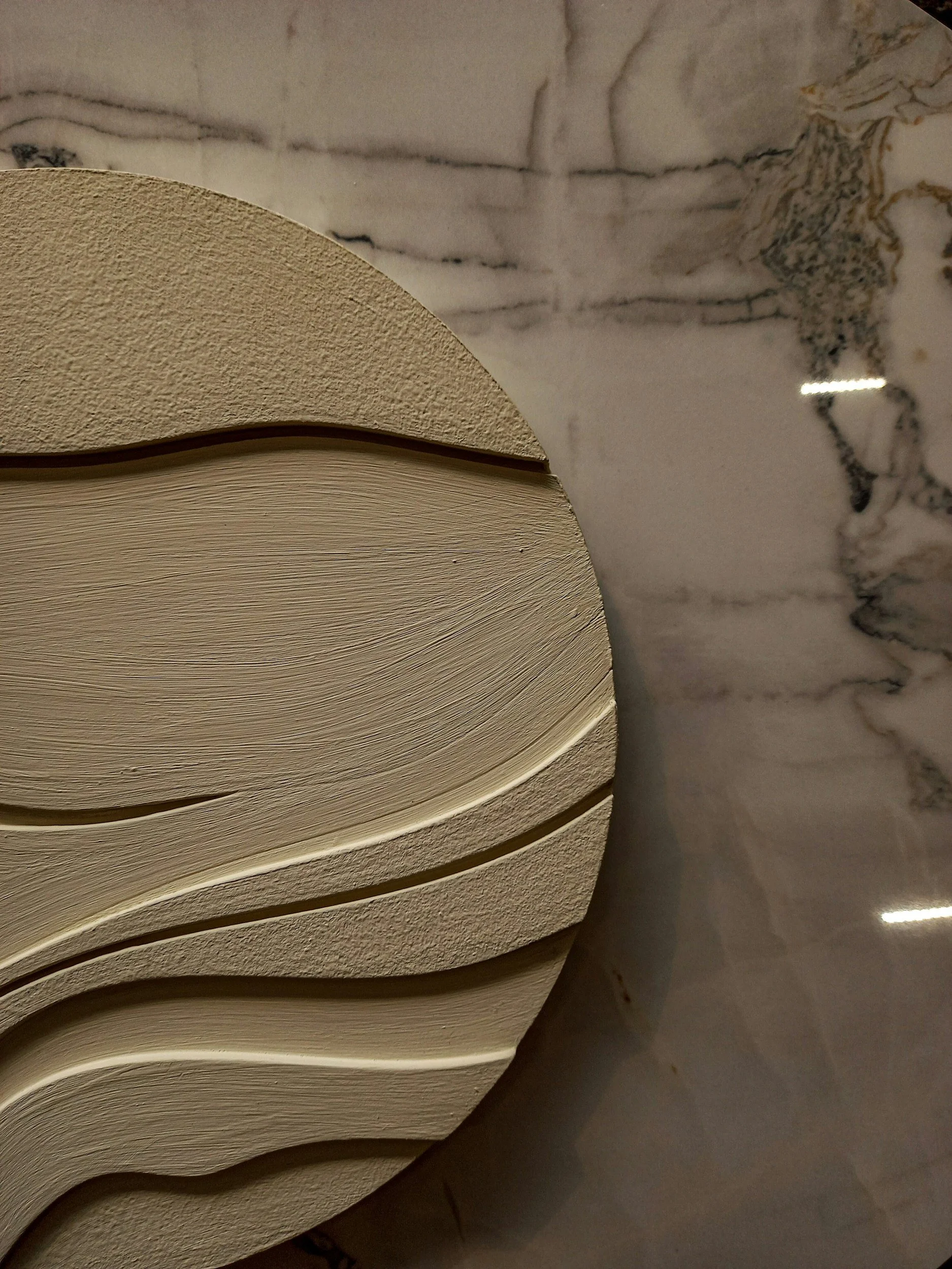 Close-up of a textured, layered beige object with curved, flowing lines on a marble surface.