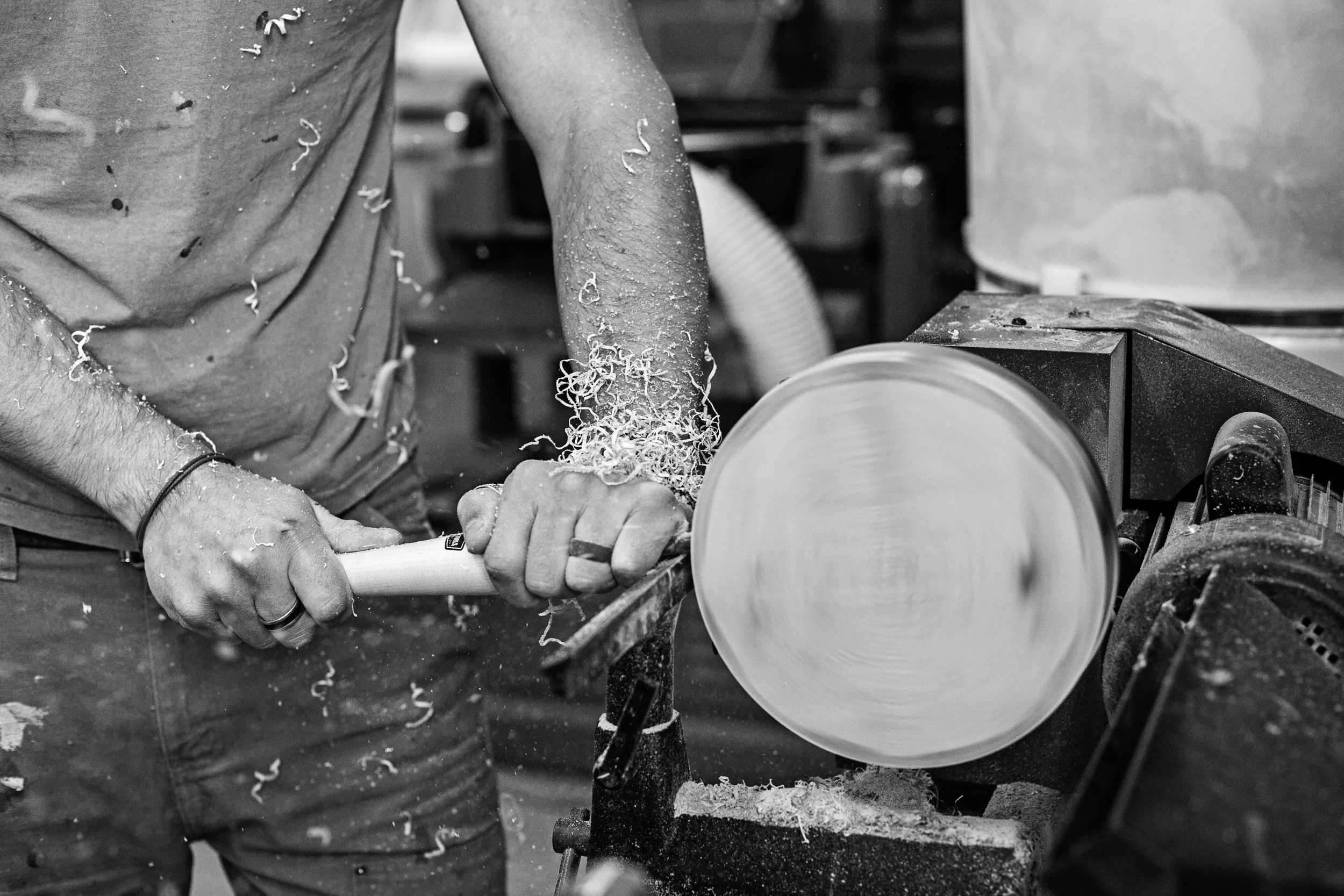 Person turning solid wood object on a turning machine in a workshop.