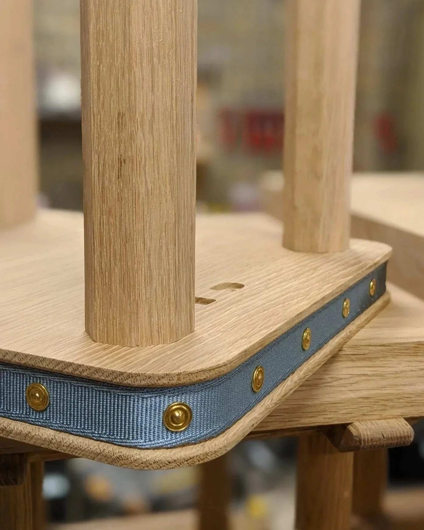 A close-up view of a wooden structure with vertical wooden dowels, a rounded wooden base, and a blue fabric trim with gold studs.