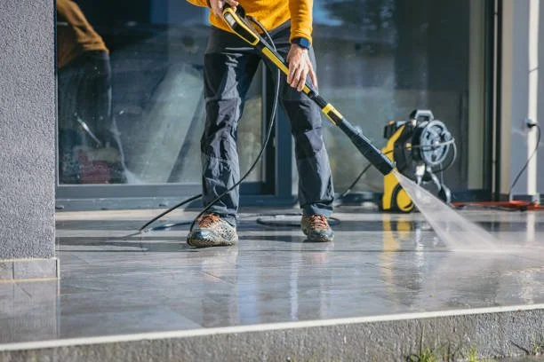 Person pressure washing a concrete surface outside a building.