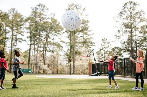 Children playing volleyball outdoors on a sunny day.