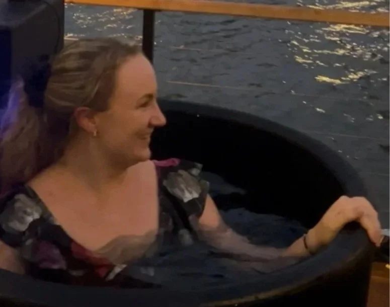 a woman in a plunge bath surrounded by water, with her head turned and smiling.