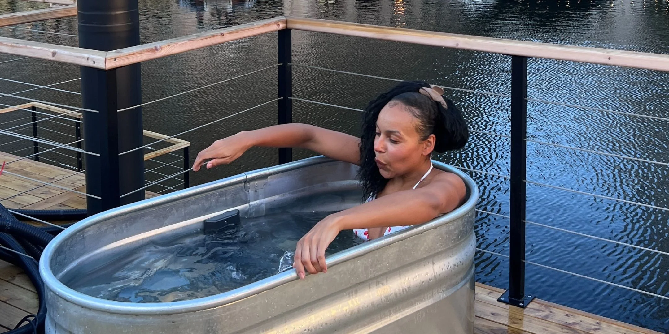 a woman breathing deeply as she sits in a cold plunge bath, on the top deck of a sauna boat - with views of water behind railings
