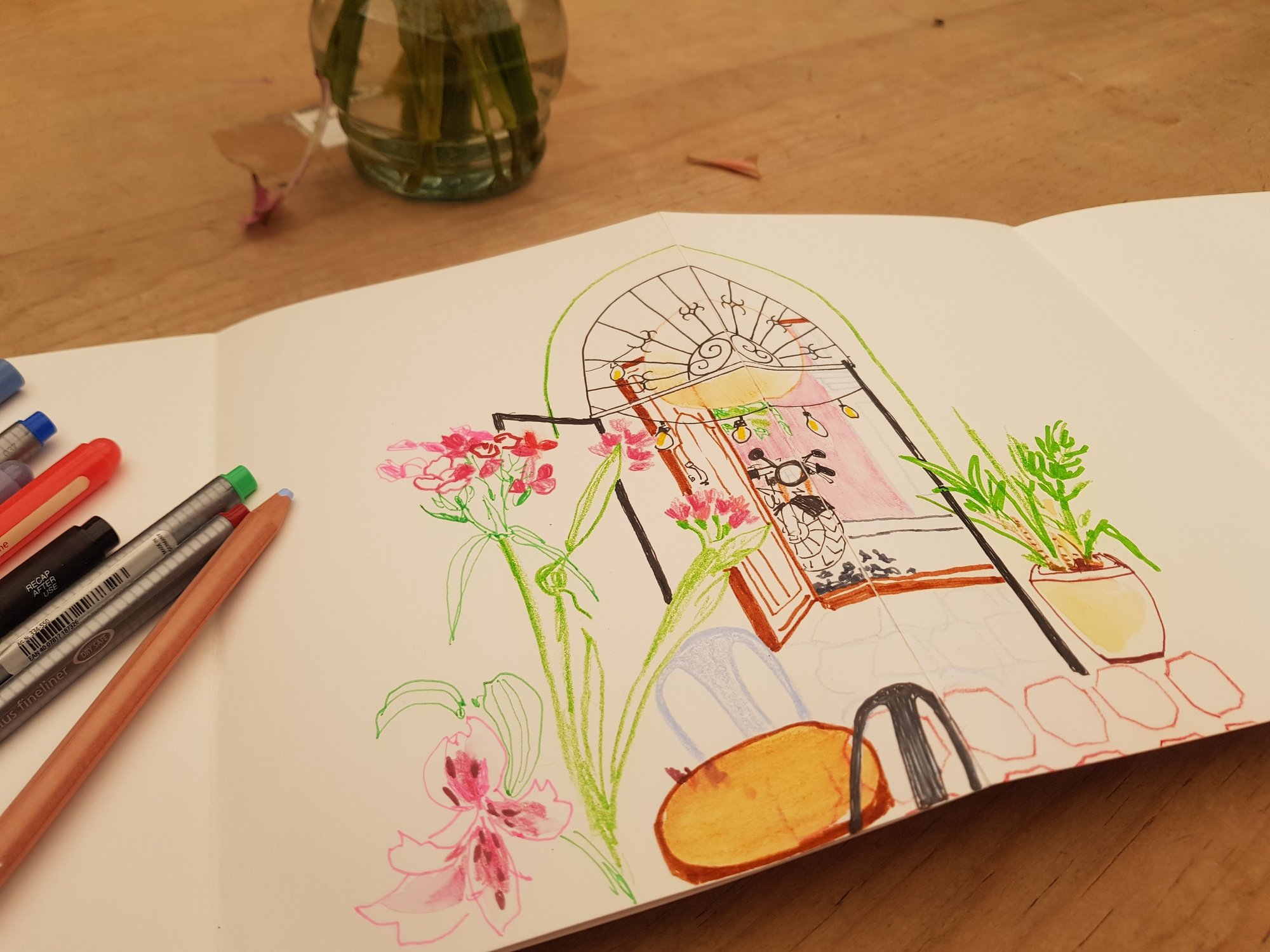 A photograph taken of Emma's sketchbook open on a table. On the page, colourful drawings of flowers can be seen.