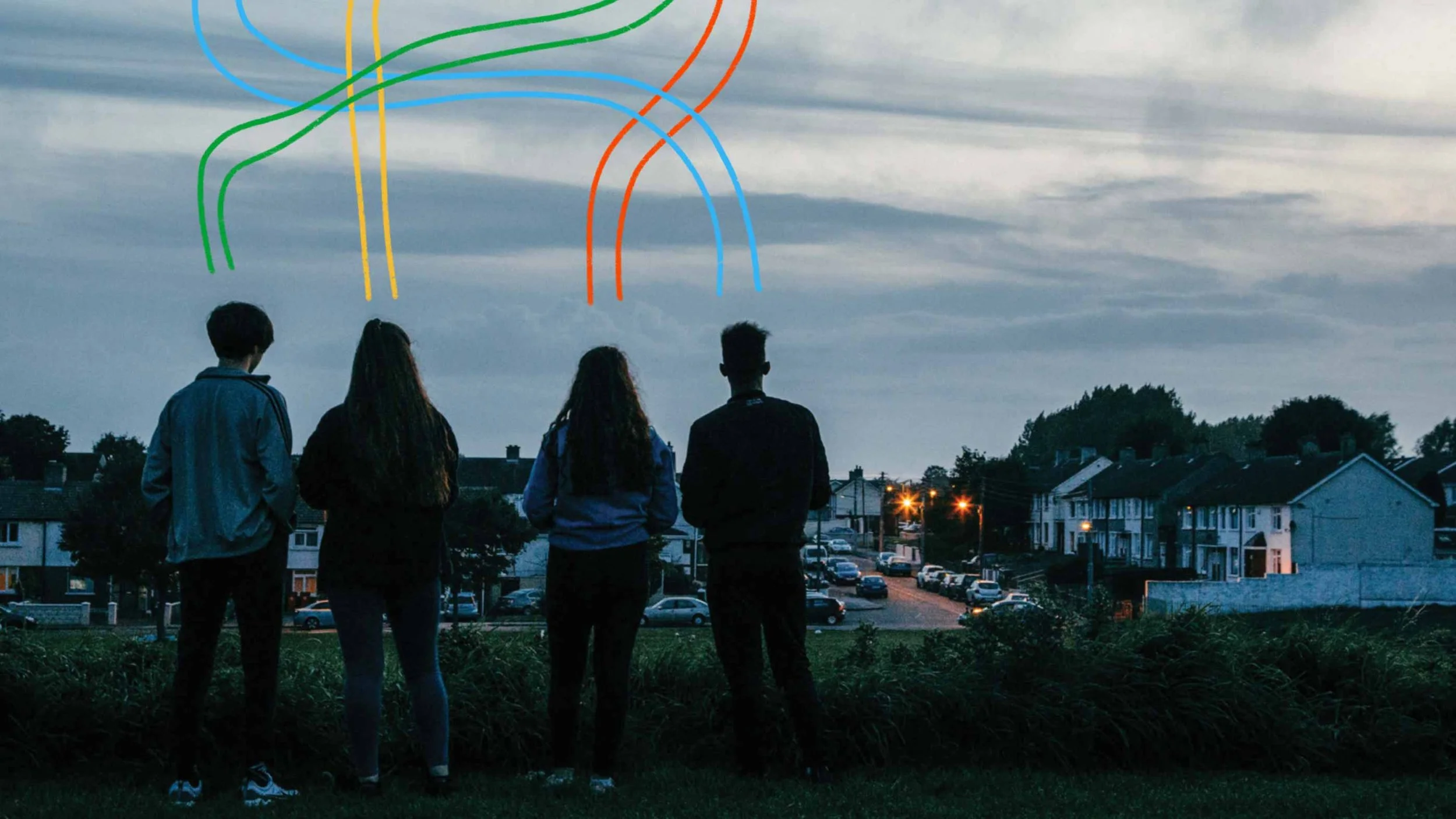 Four young people stand outdoors at dusk, facing away from the camera, with a suburban neighborhood in the background. The sky is cloudy with blue-gray hues, and colorful light trails are overlaid in the sky.