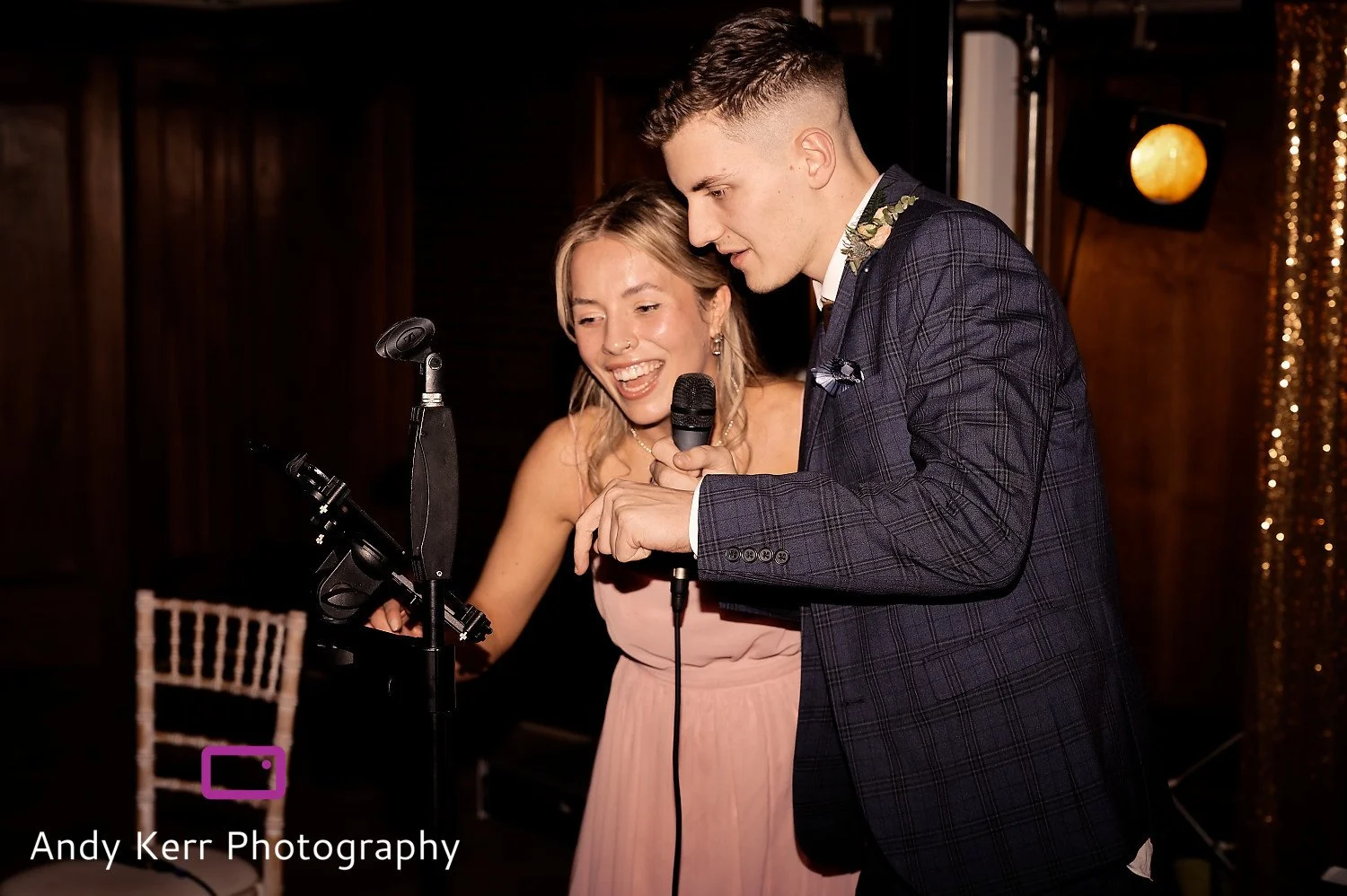 A man and woman are singing into a microphone during a wedding reception.