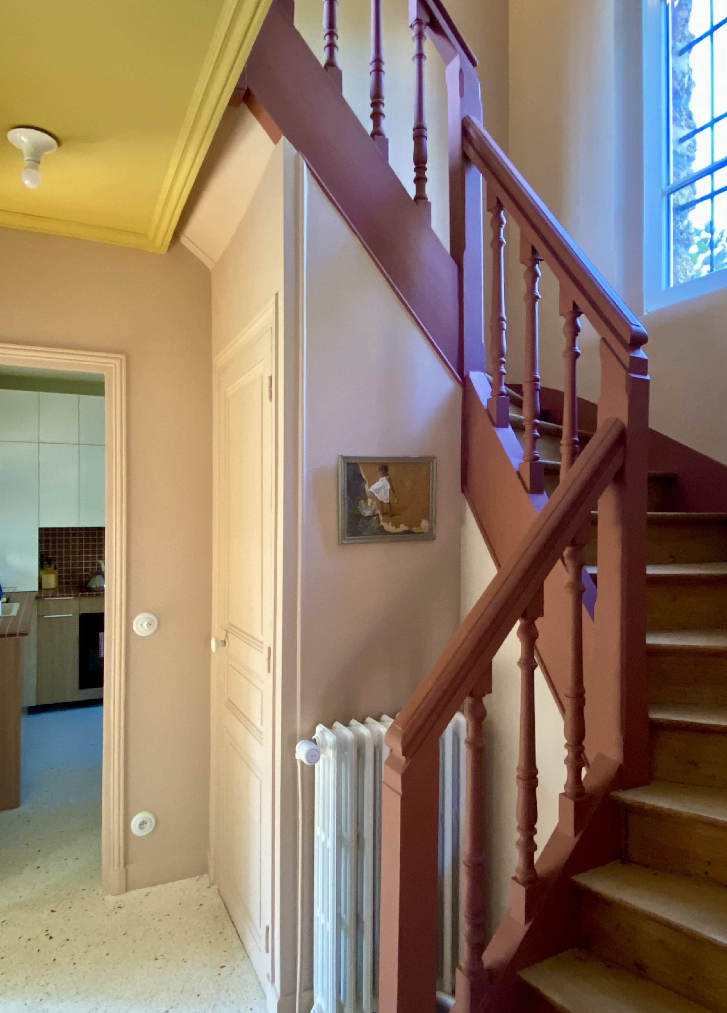 Entrée d'une maison meulière avec terrazzo aus ol, escalier bordeaux et murs roses, plafond jaune