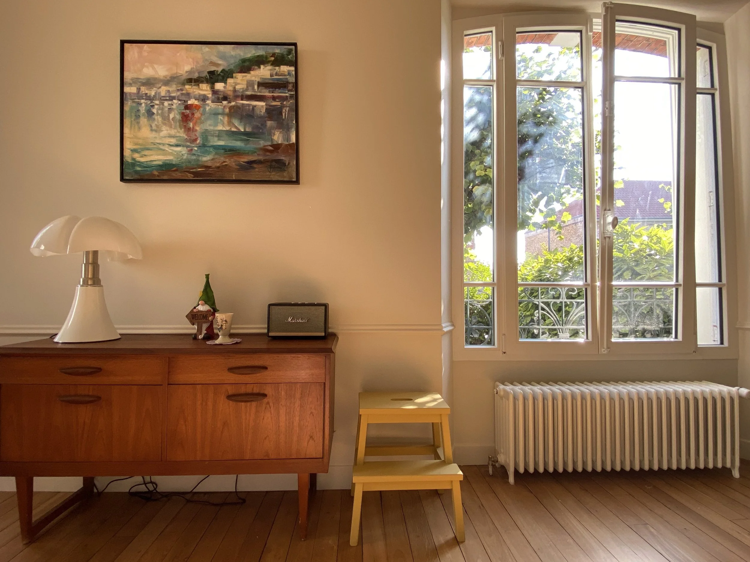 Salon avec moulures et parquet massif, radiateur en fonte, fenêtre cintrée, tableau, enfilade scandinave chinée, lampe design et tabouret jaune