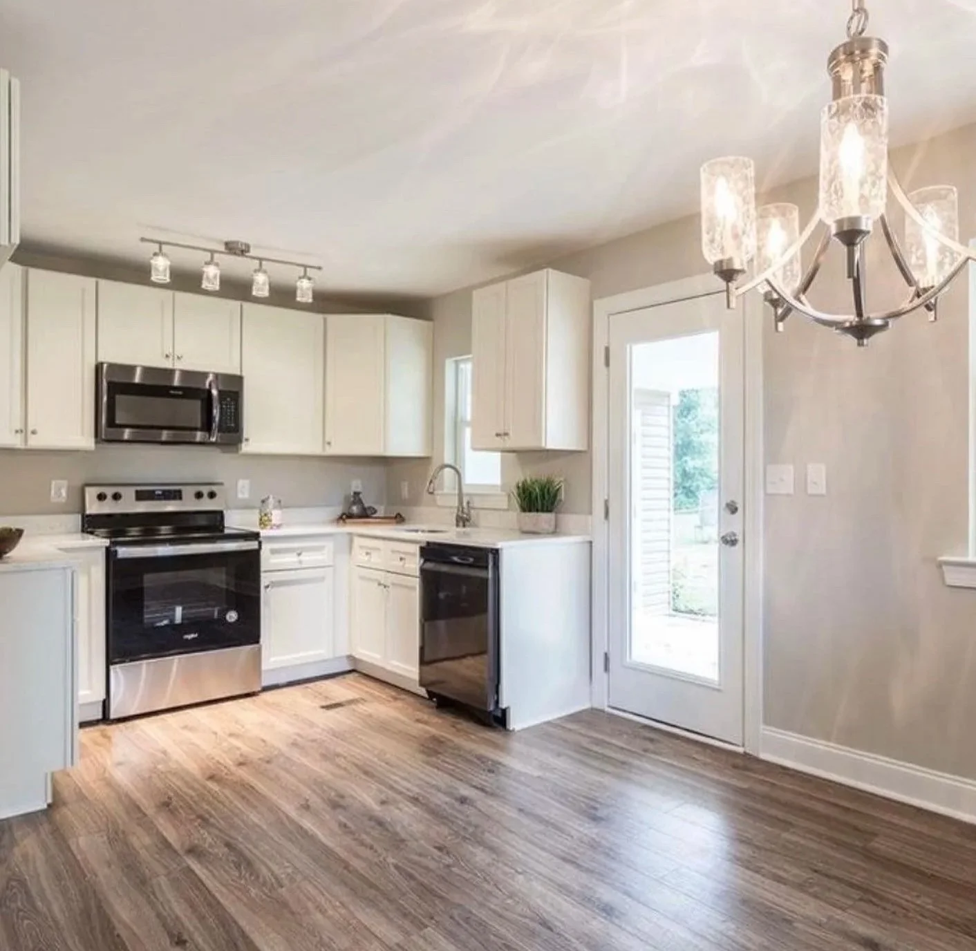 Kitchen with white cabinets, stainless steel appliances, wooden flooring, a door with a window leading outside, and a chandelier light fixture.