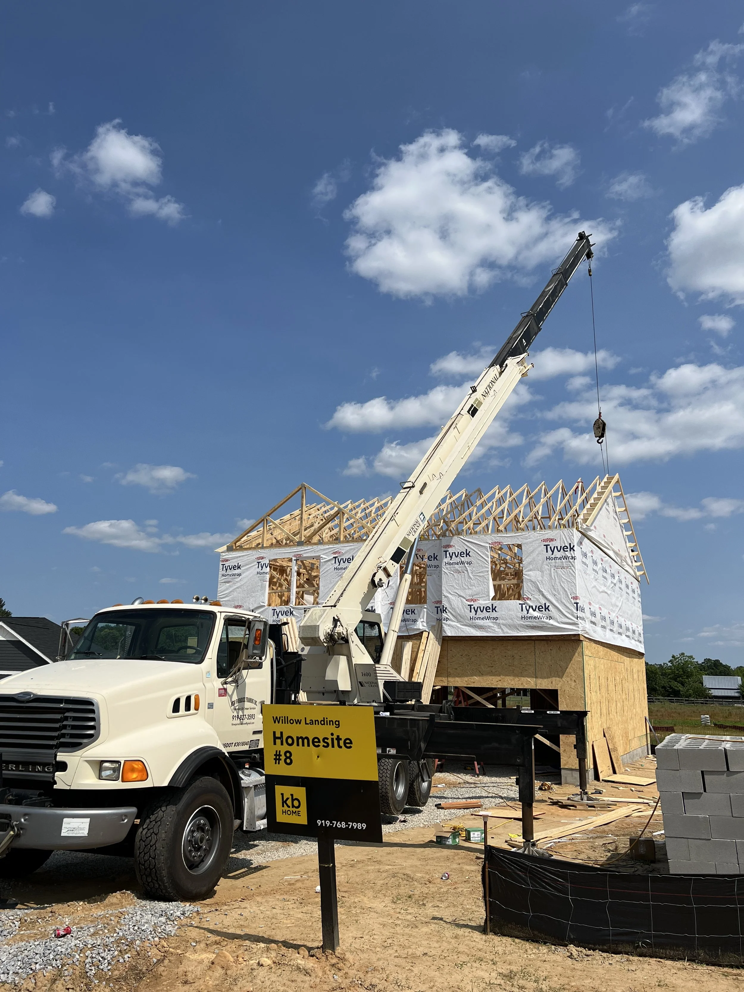 Construction site with a crane building a house, marked as Willow Landing Homesite #8, under a partly cloudy sky.