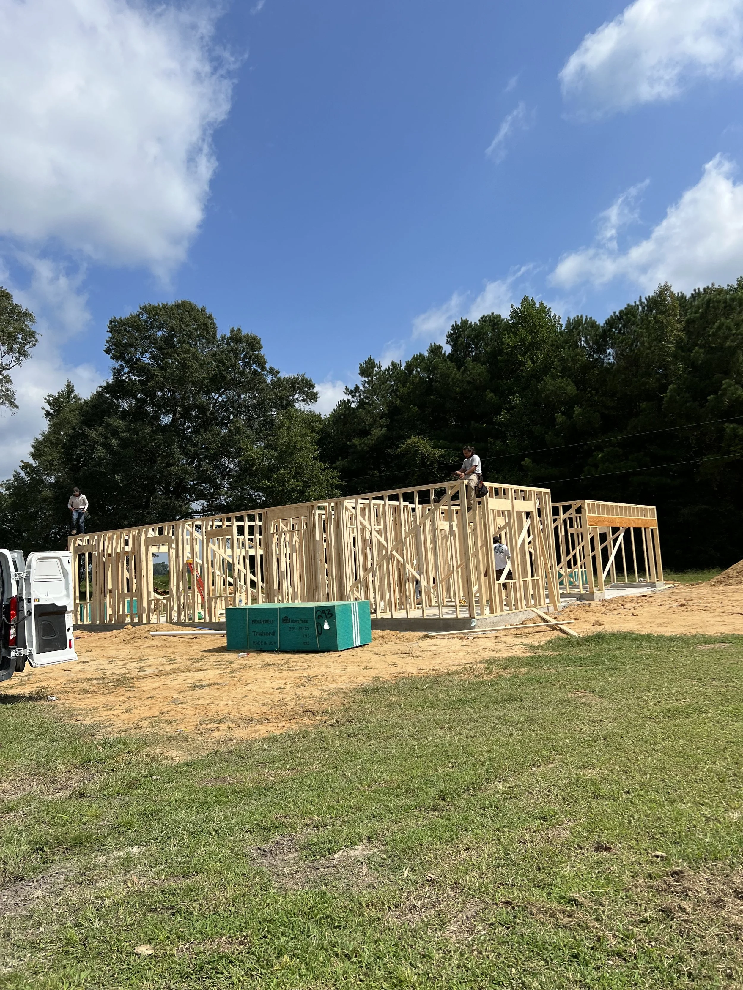 Construction workers building a wooden house frame outdoors on a sunny day.