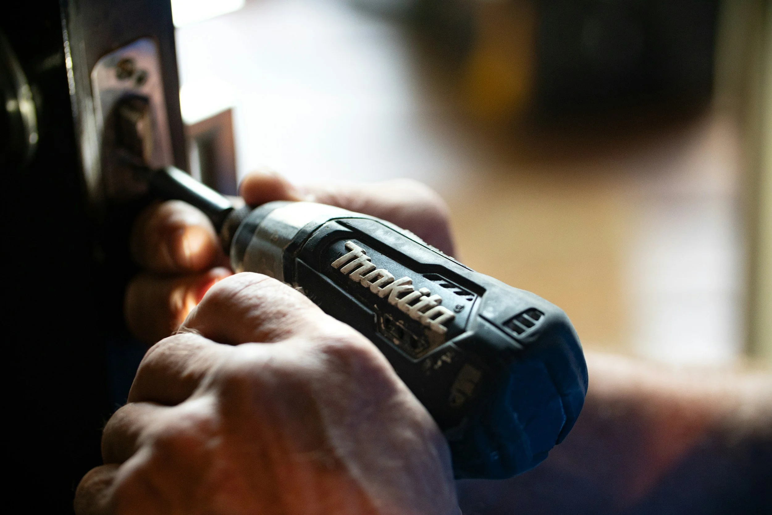 Close-up of a person using a black and gray power drill to screw into a wall outlet.