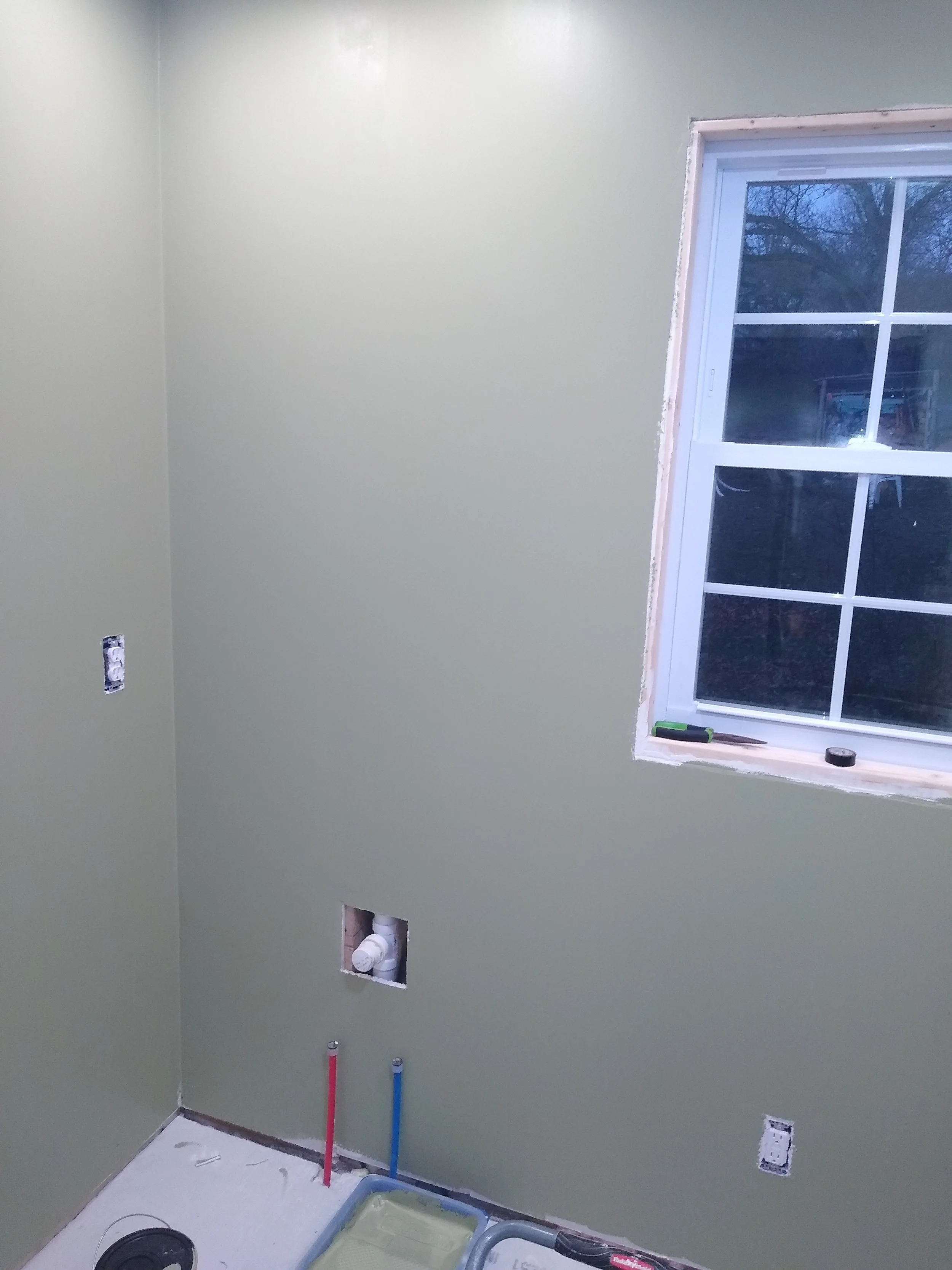 Interior of a room under renovation with pale green walls, an open window, and plumbing pipes.