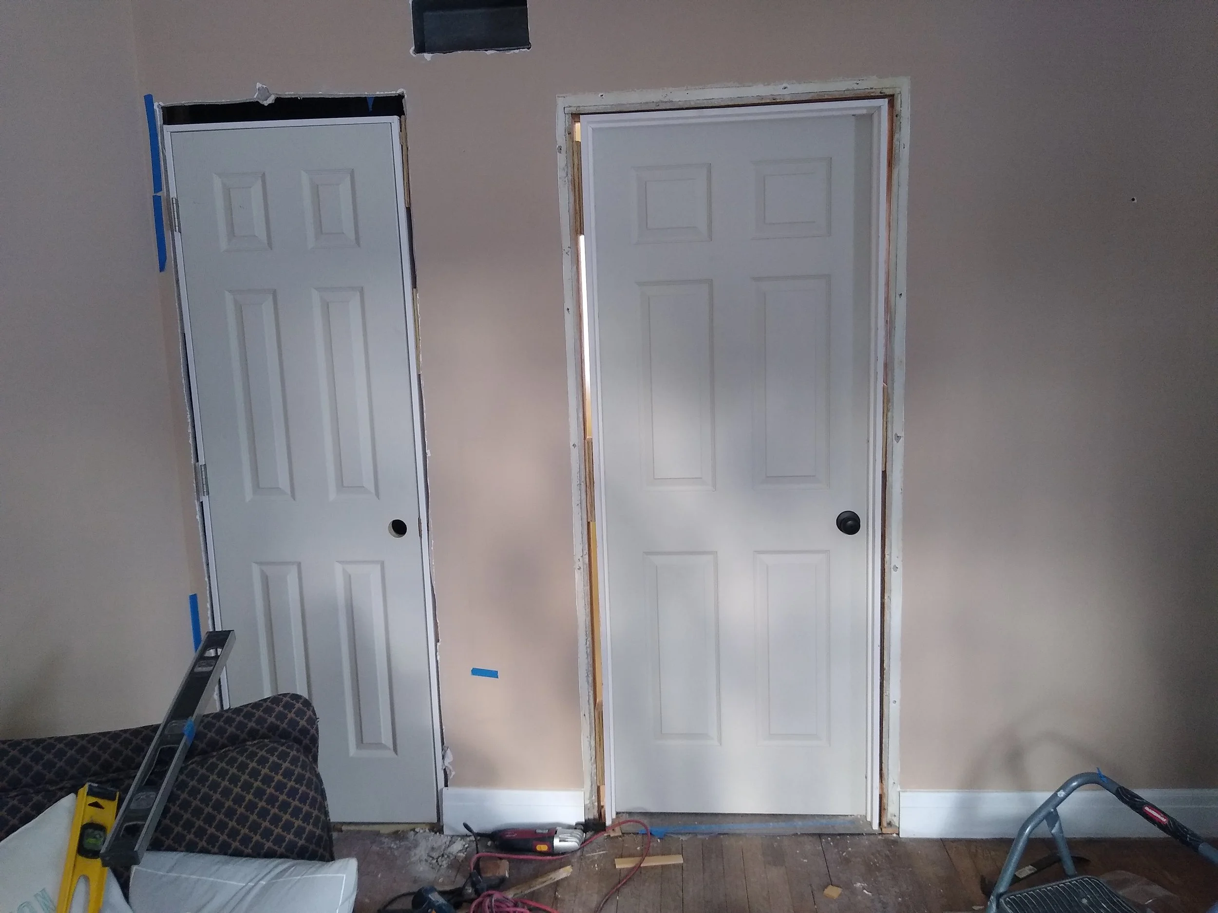 Two interior doors in a room under renovation, with unfinished trim and construction tools on the floor.