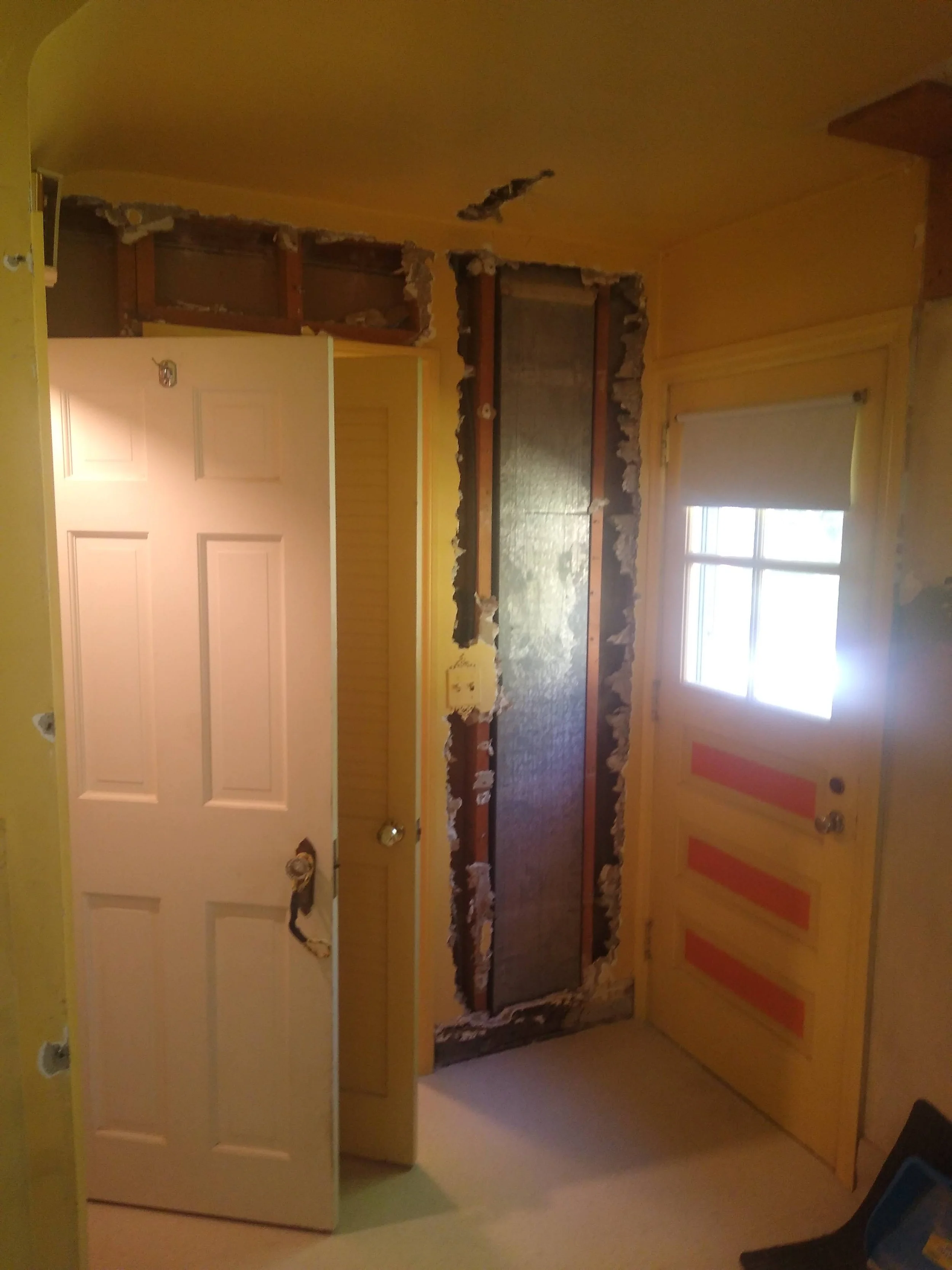 Interior of a room under renovation, with a partially removed wall and exposed framing.