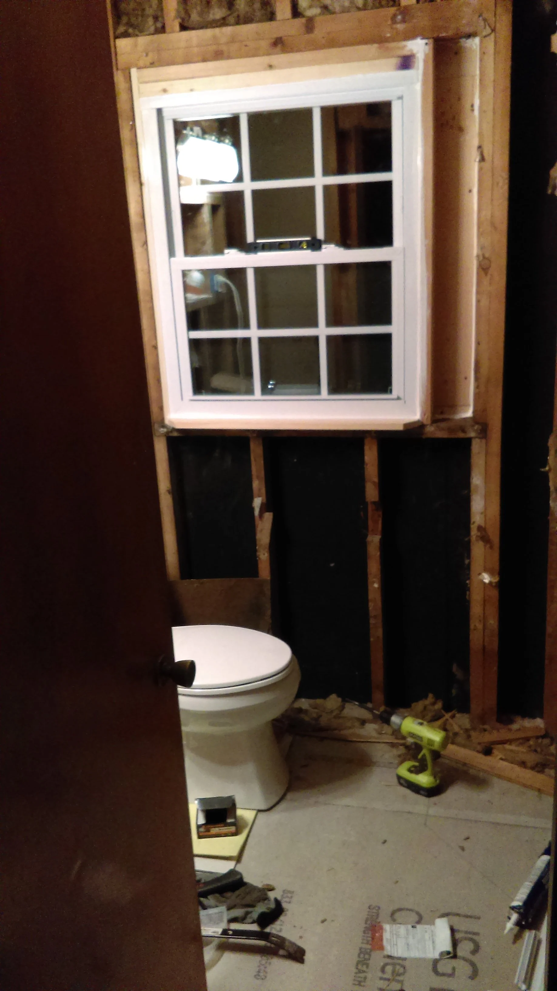 Bathroom in progress with exposed wall studs, window, toilet, and construction tools.