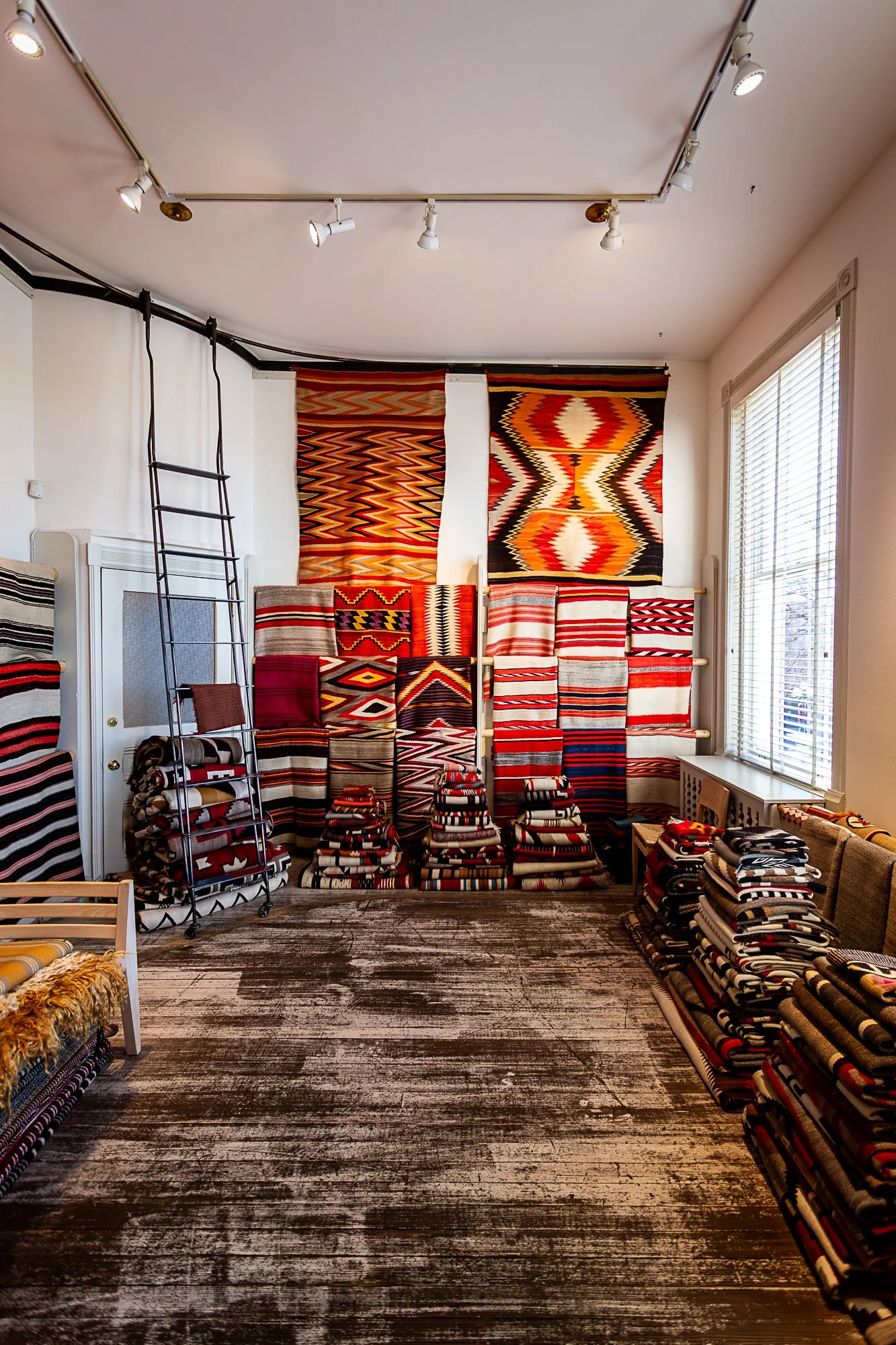 Display of woven textiles and rugs with geometric patterns in red, black, white, and yellow tones in a store interior in Santa Fe New Mexico.